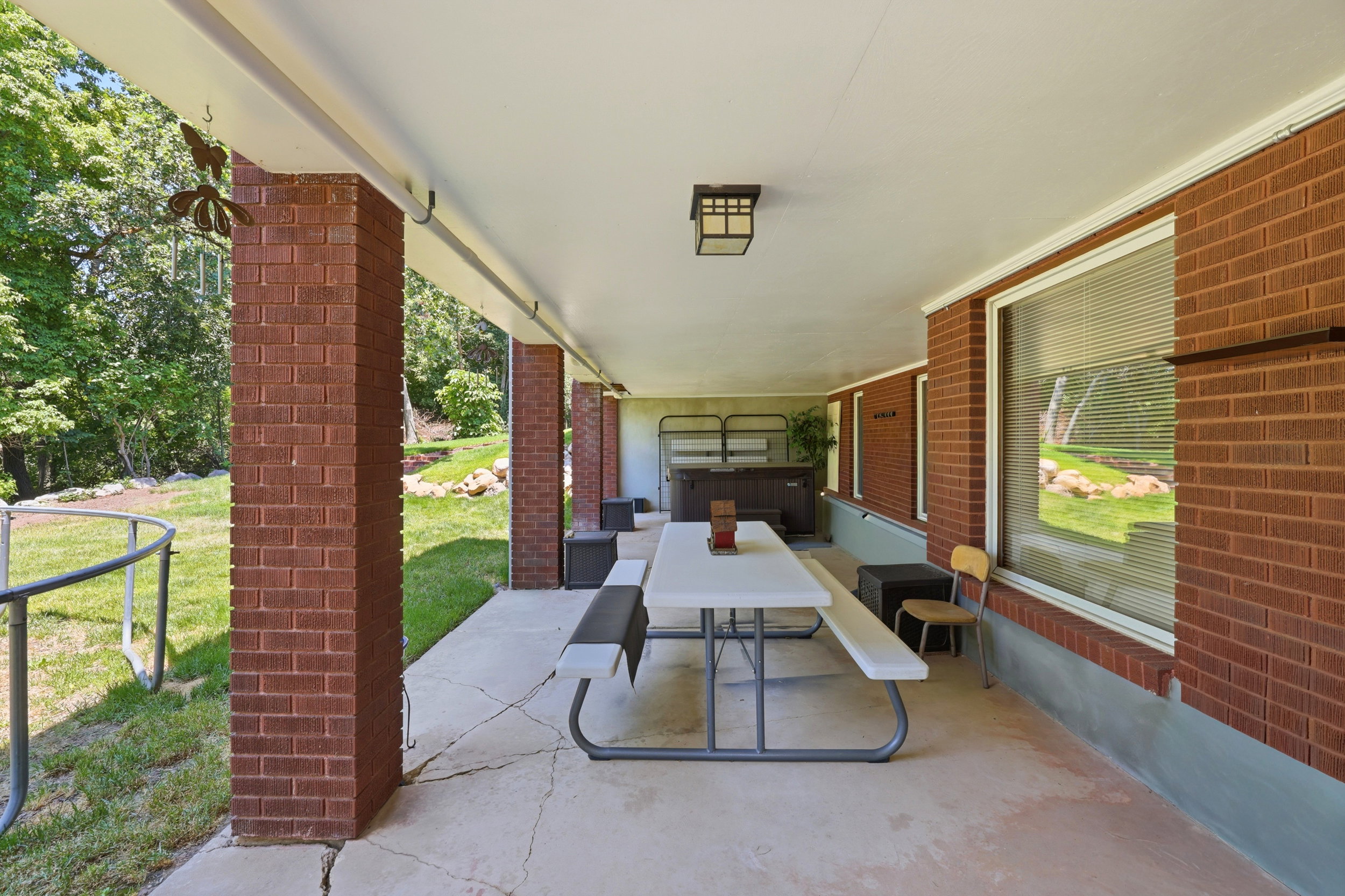 Covered patio featuring brick pillars, an overhead light fixture, large windows, and a built-in hot tub