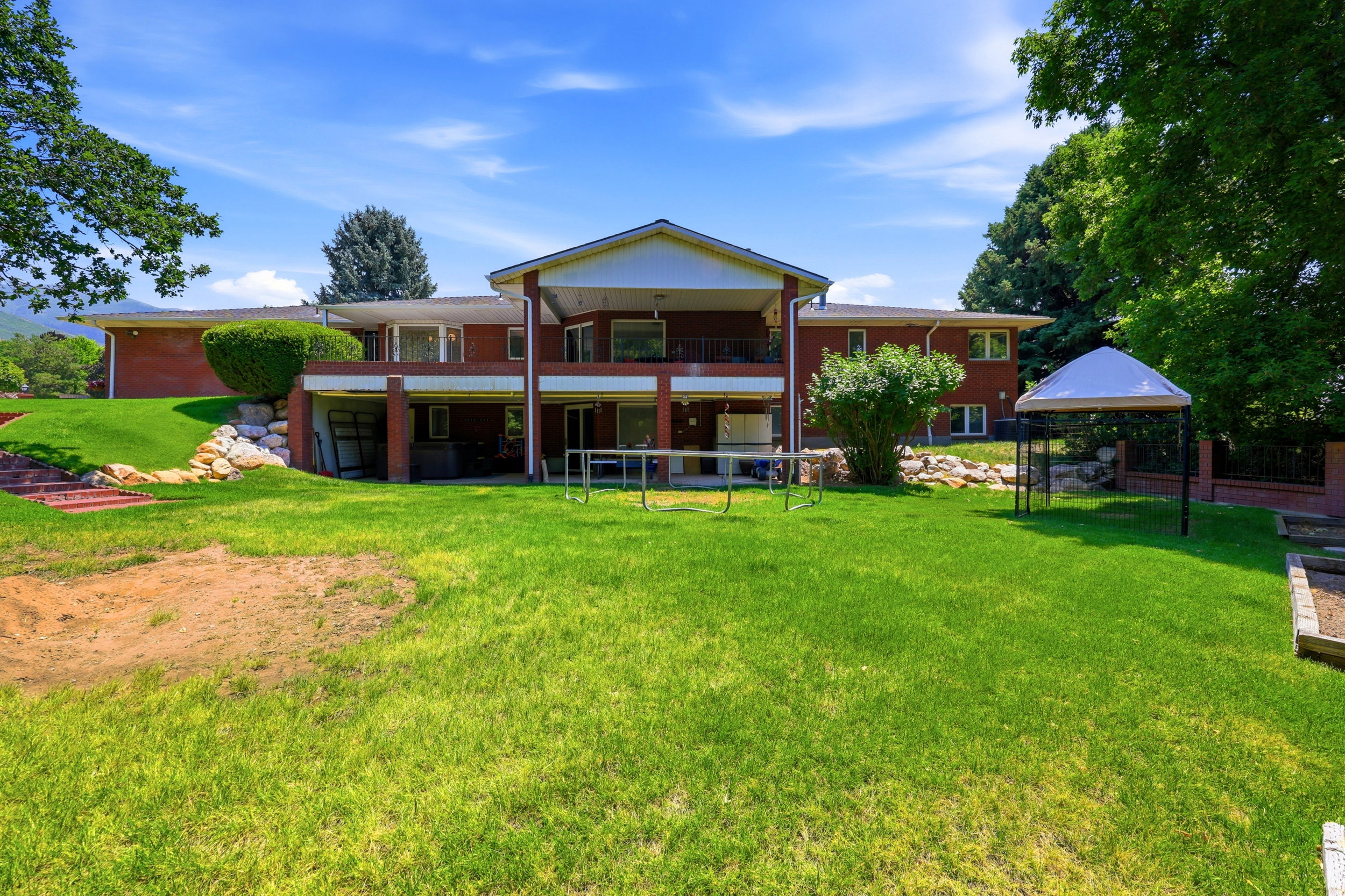 Expansive green lawn with a two-story brick exterior featuring a covered upper-level balcony and a covered lower-level patio