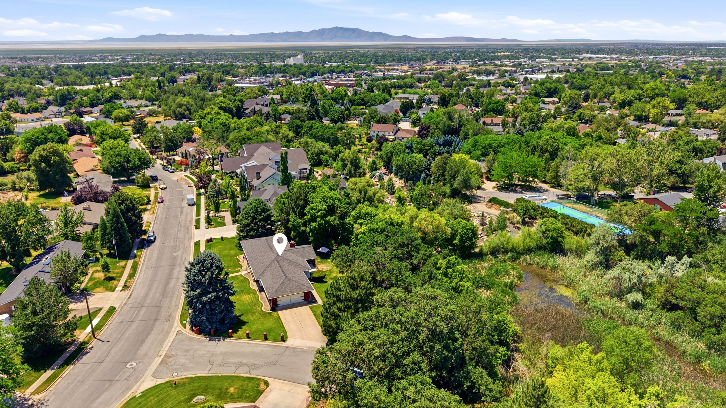 Property situated on a street with mature trees and green landscaping, featuring a paved driveway and a two-car garage
