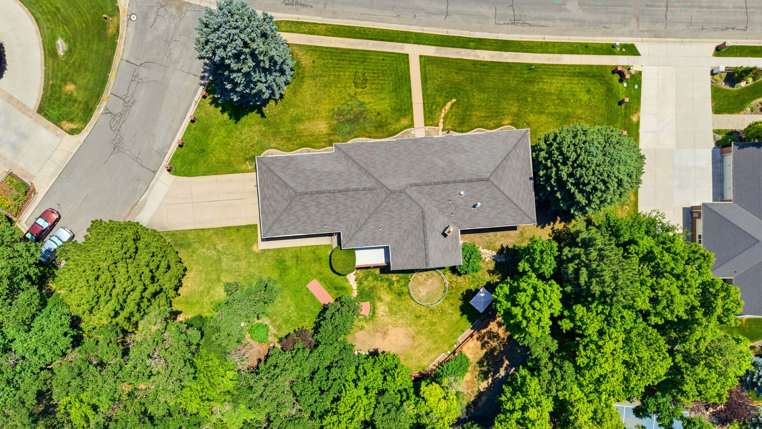 Overhead property view featuring a gabled roofline, expansive surrounding greenery, mature trees, a defined driveway, and a paved street