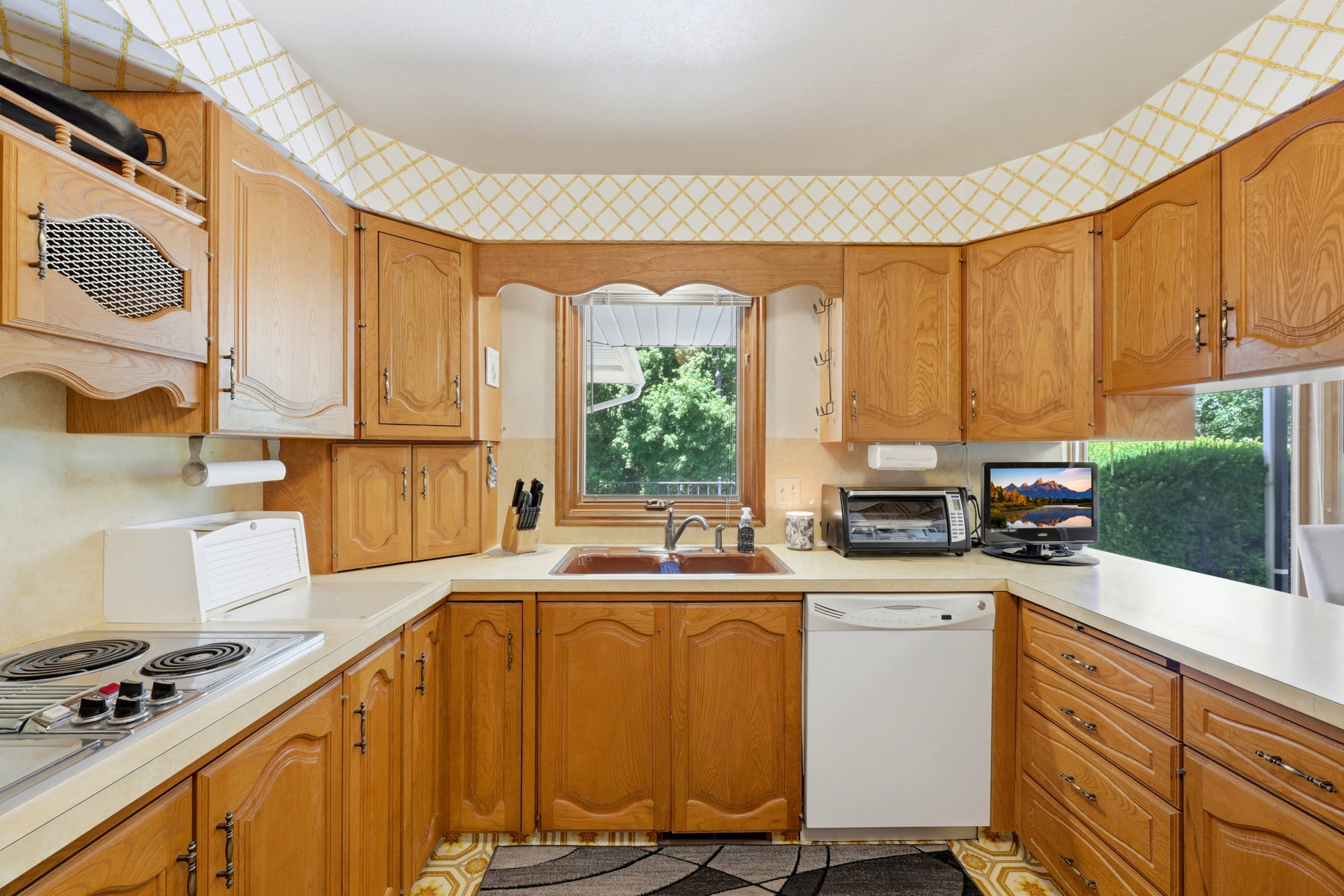U-shaped kitchen featuring wood-finish cabinetry, a ceramic cooktop, and a built-in dishwasher