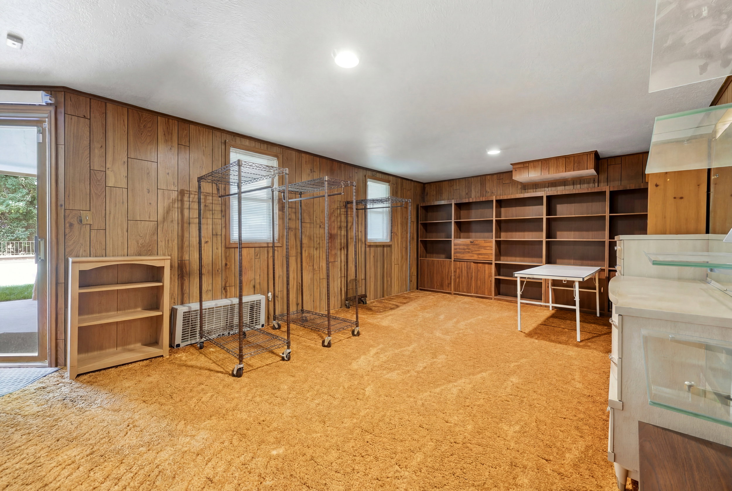 Spacious room featuring wood paneling, built-in shelving, plush carpeting, and recessed lighting