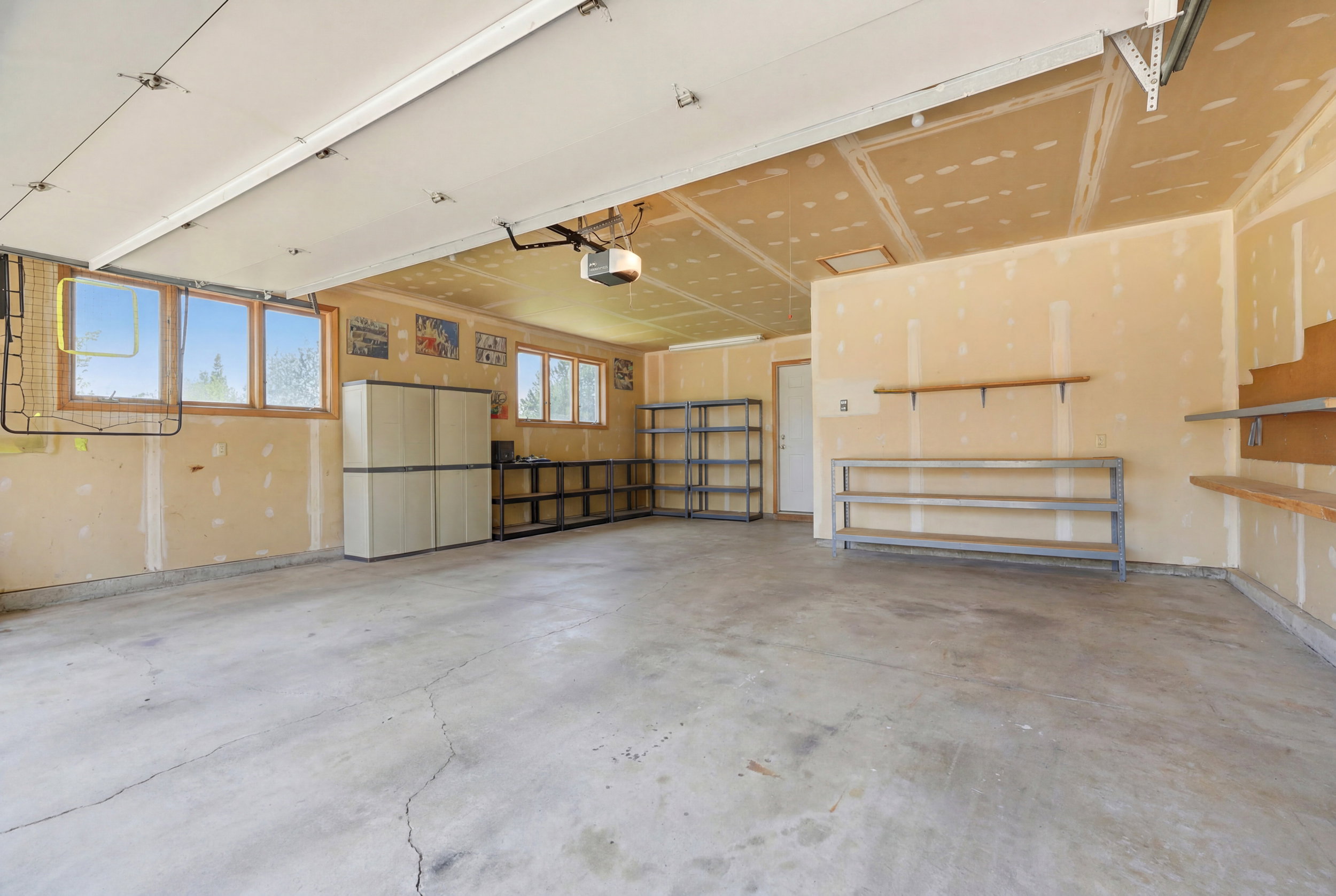 Spacious garage with multiple windows for natural light, concrete flooring, built-in shelving, and exposed ceiling joists