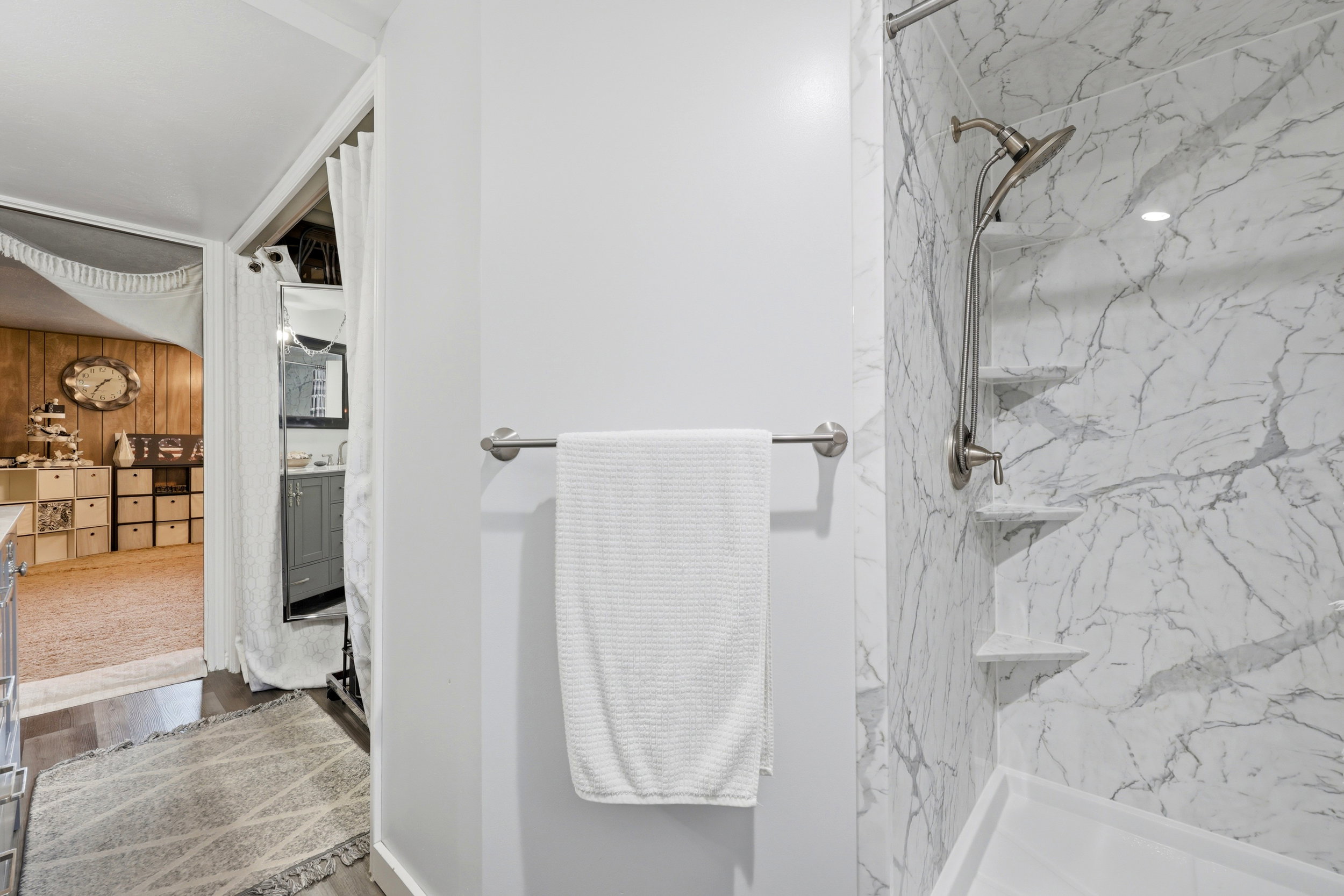 Shower featuring white marble-patterned paneling, built-in corner shelving, and a brushed nickel shower fixture