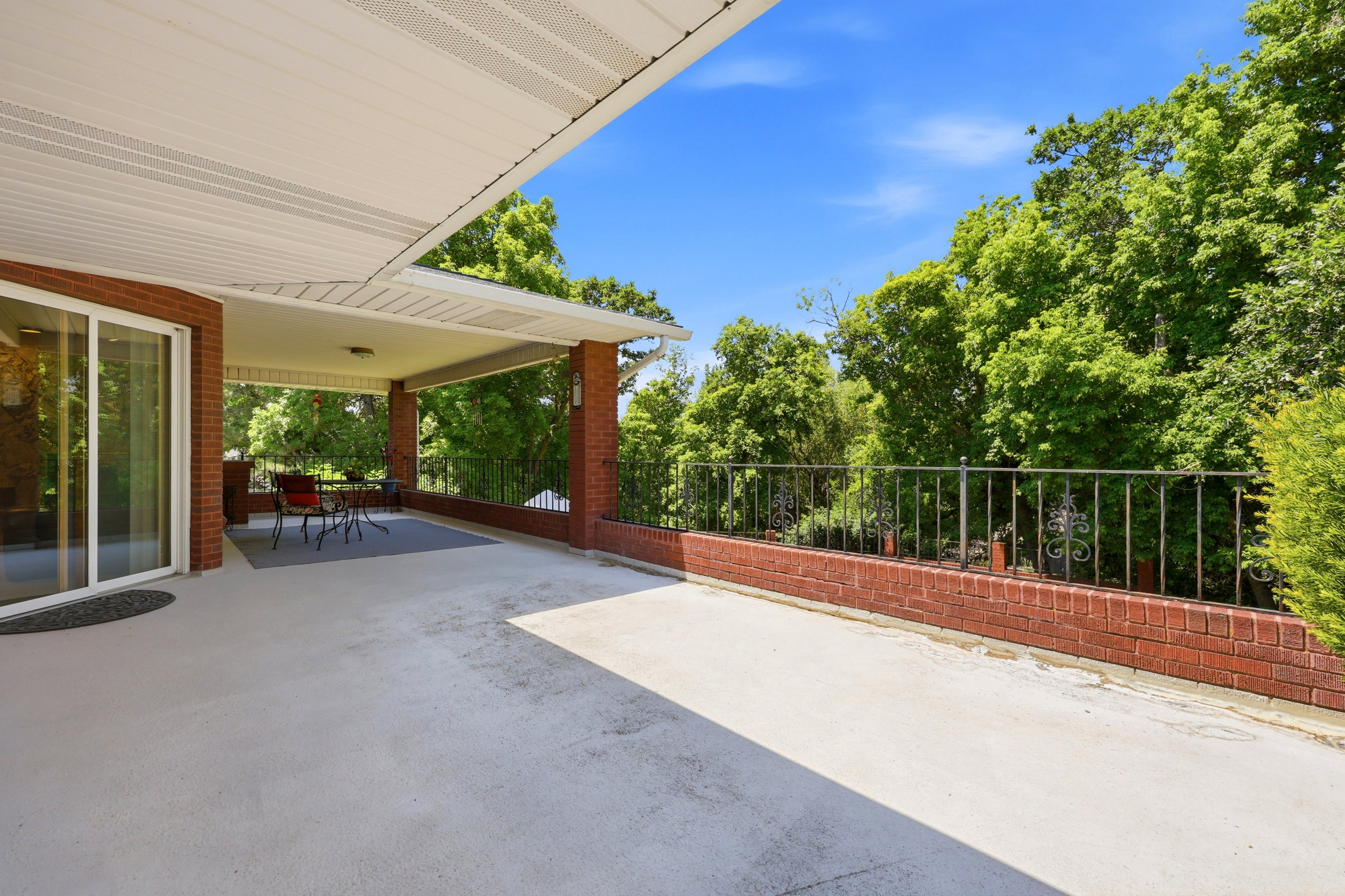 Expansive outdoor patio area featuring a covered section with recessed lighting, brick pillars, and a decorative wrought iron railing