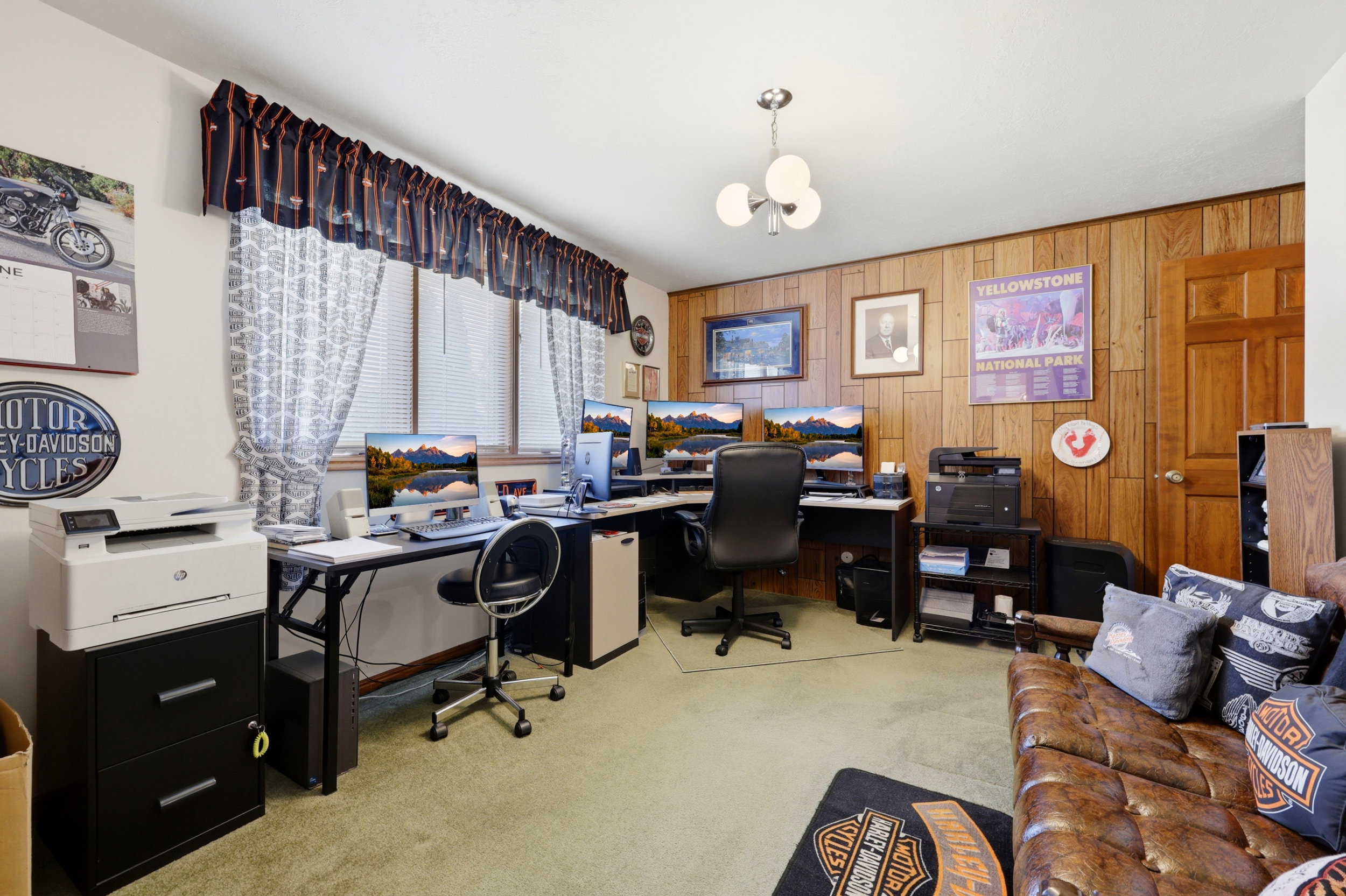 Room featuring wood paneling, a large window with blinds and valance, carpet flooring, a ceiling-mounted light fixture, and a solid wood door