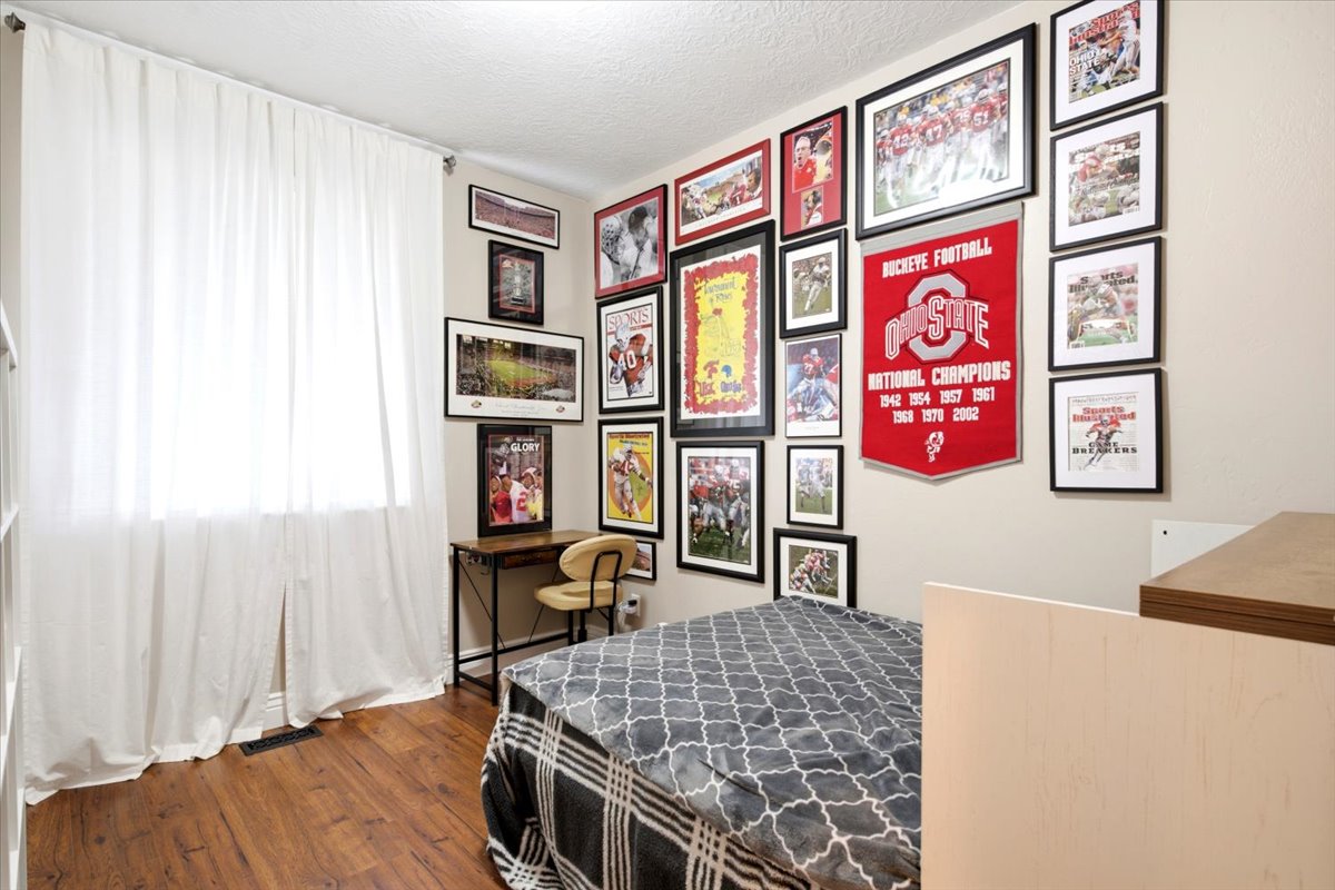 Bedroom featuring wood-finish flooring, a window with white drapes, and neutral wall paint