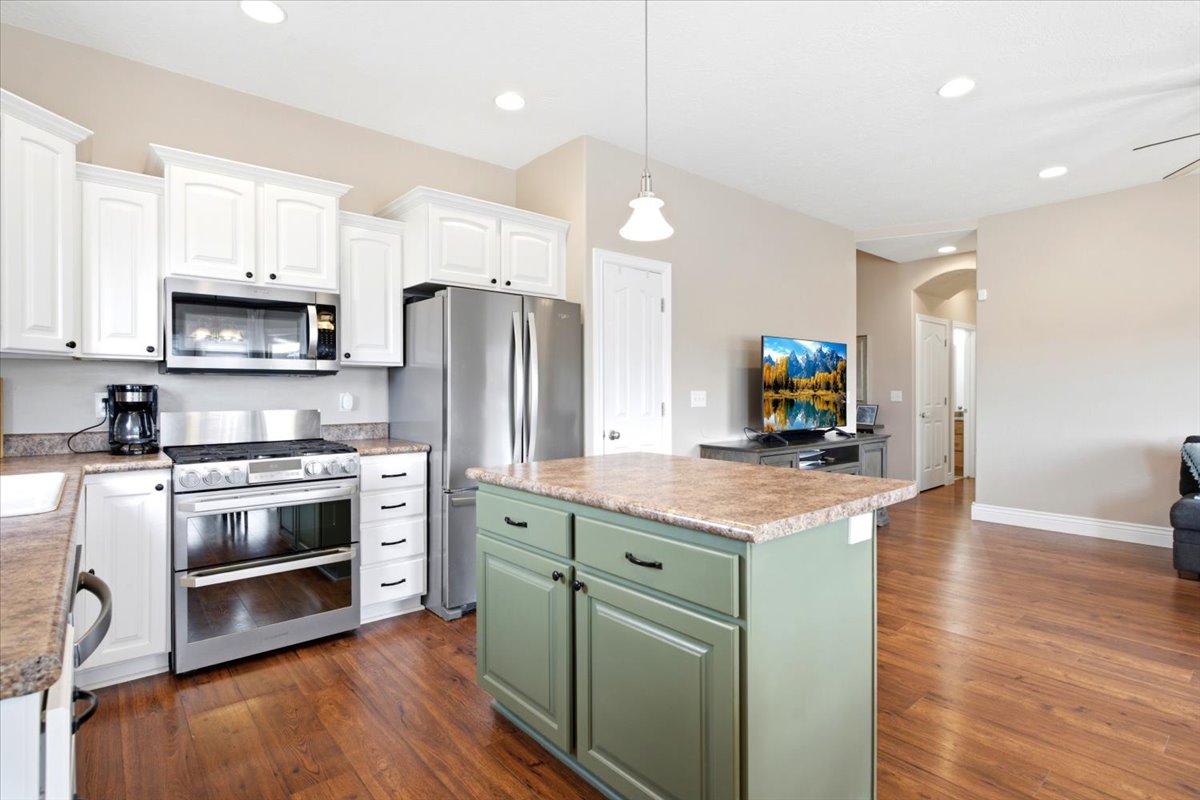 Kitchen featuring white cabinetry, stainless steel appliances, a center island with a composite countertop, and wood-finish flooring