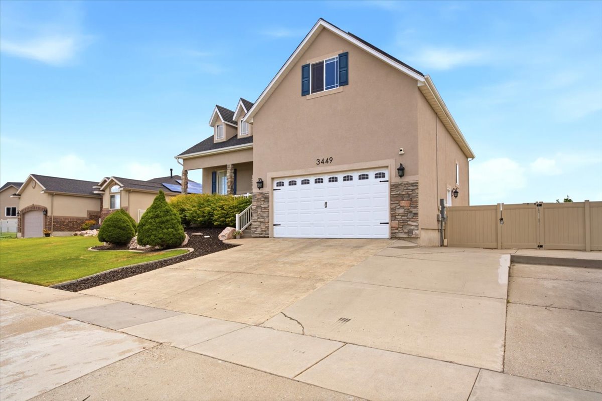 Stucco exterior featuring a two-car garage with white paneled door, stone veneer accents, and a paved driveway
