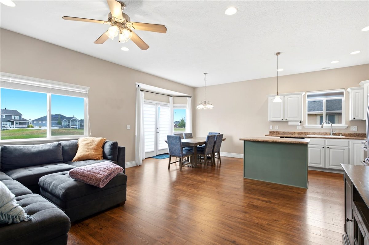 Open-concept living area featuring wood-finish flooring throughout, a kitchen island with a contrasting base, white cabinetry, and recessed lighting