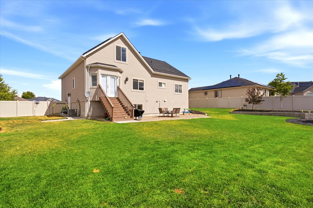 Expansive grassy backyard featuring a paved patio area, multi-tiered landscaping, and a privacy fence