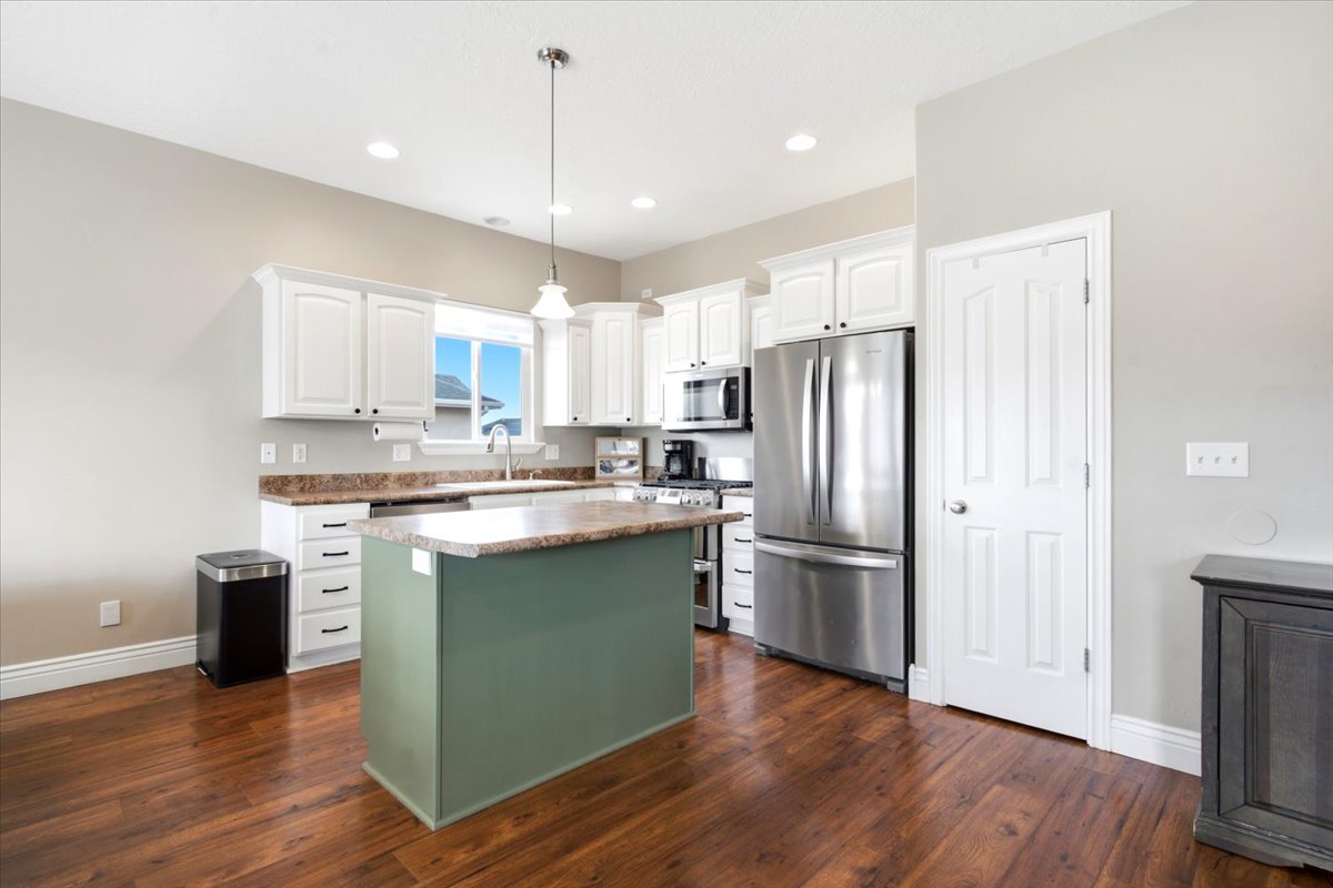 Kitchen featuring white cabinetry, a central island with a contrasting base, wood-finish flooring, and stainless steel appliances