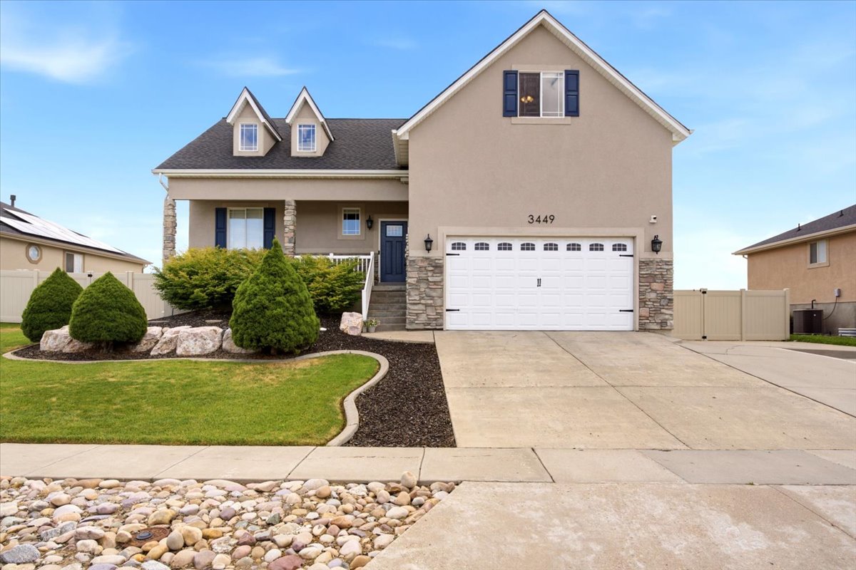 Stucco-clad exterior with stone accents, a two-car garage, a covered front porch, and dormer windows