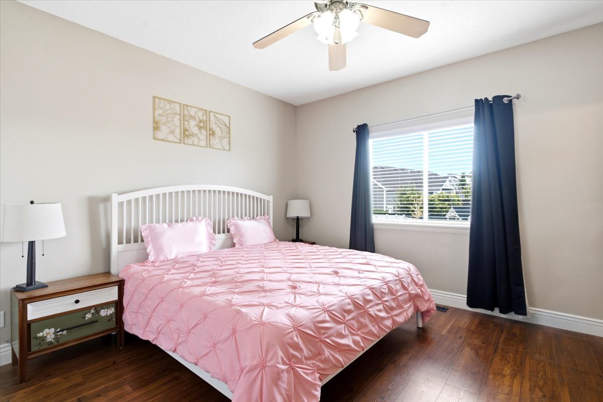 Bedroom featuring wood-finish flooring, a ceiling fan with integrated lighting, a window with horizontal blinds, and neutral wall paint