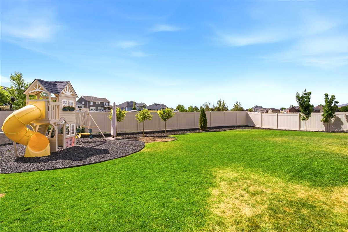 Expansive lawn area featuring a perimeter fence, mature trees, and a dedicated play structure with slides and swings