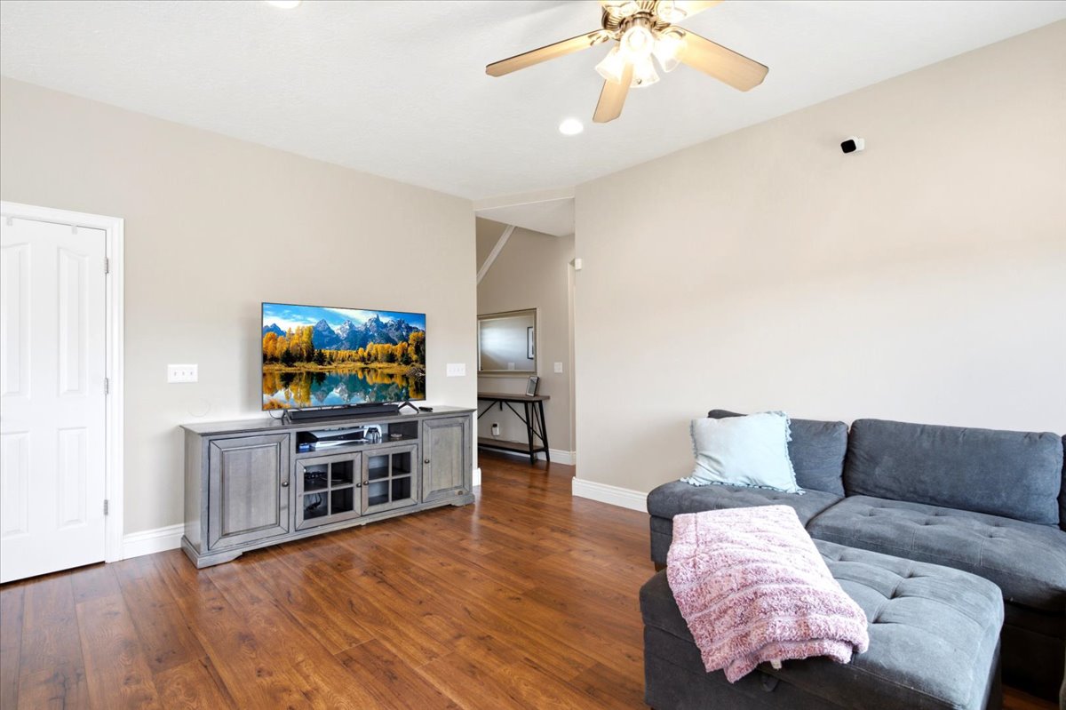 Living area featuring wood-finish flooring, neutral wall paint, and a ceiling fan with integrated lighting