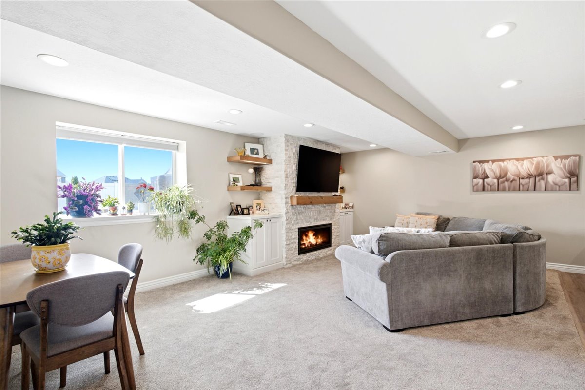 Spacious living area featuring recessed lighting, a large window, a built-in fireplace with stone surround, a wood mantle, and built-in cabinetry with open shelving