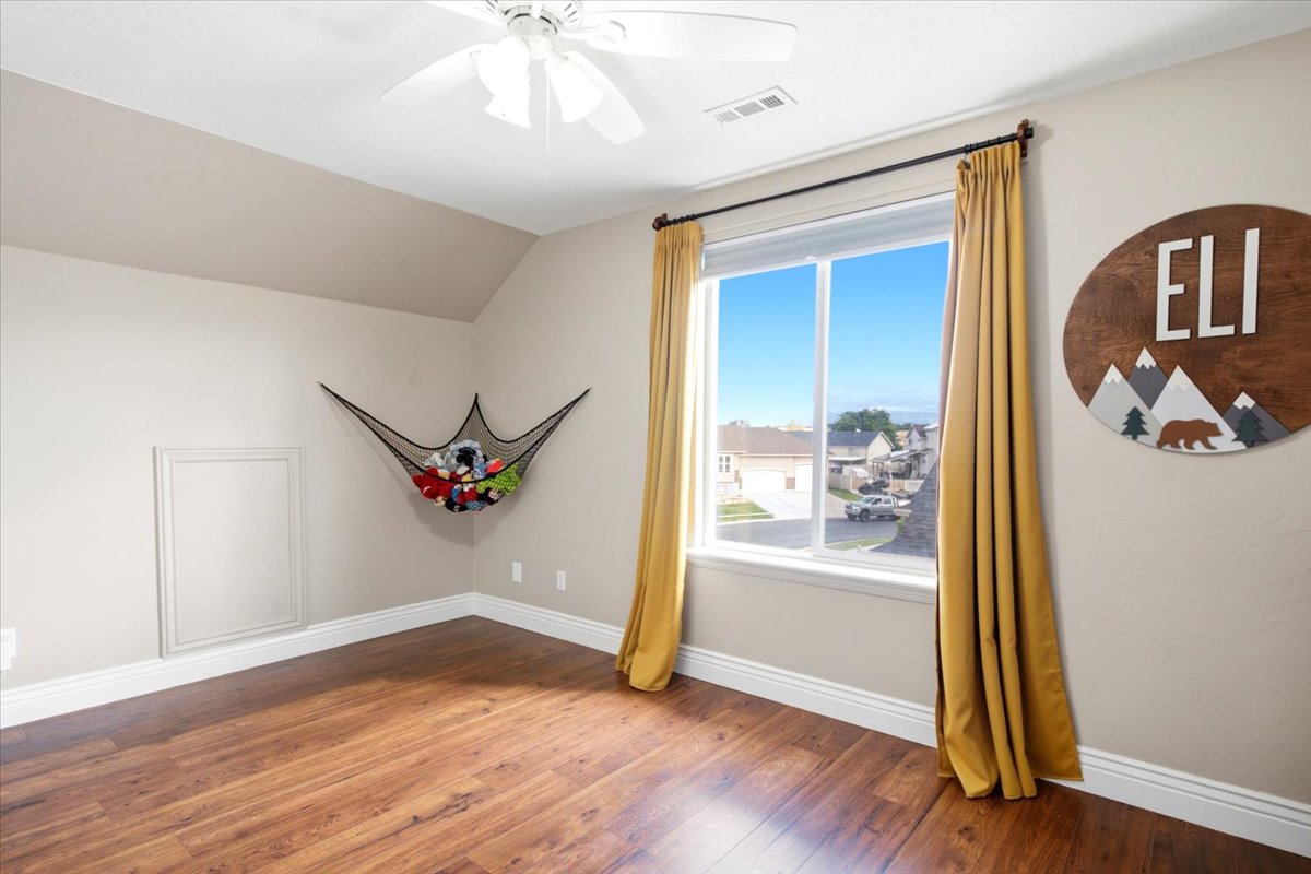 Spacious room featuring wood-finish flooring, a large window with natural light, a ceiling fan, and white baseboards