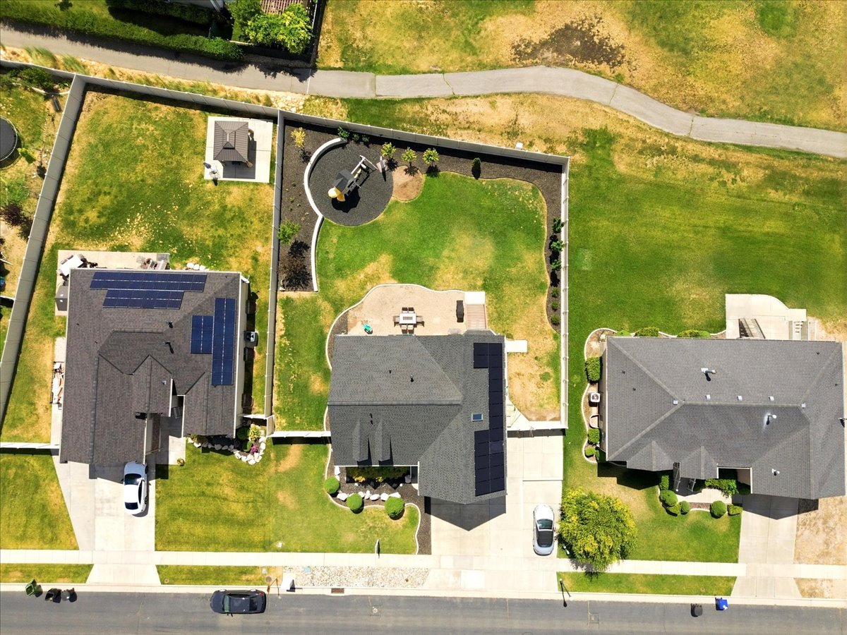 Aerial perspective showcasing the property's expansive green lawn, shaded patio area, and paved driveway