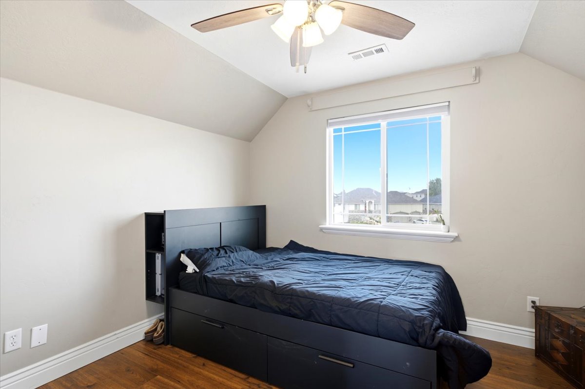 Angled ceilings complement the wood-finish flooring in this room featuring a window with natural light, a ceiling fan with integrated lighting, and white baseboards