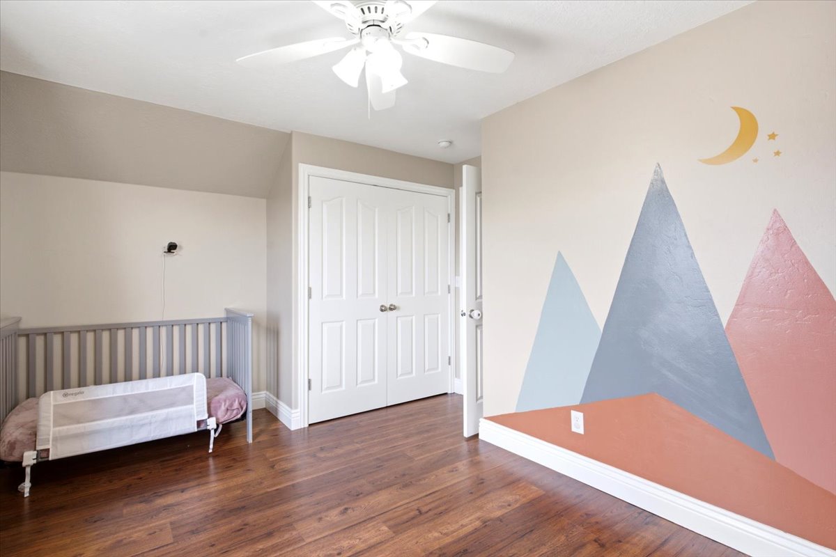 Spacious room featuring wood-finish flooring, a ceiling fan, and white paneled bifold closet doors