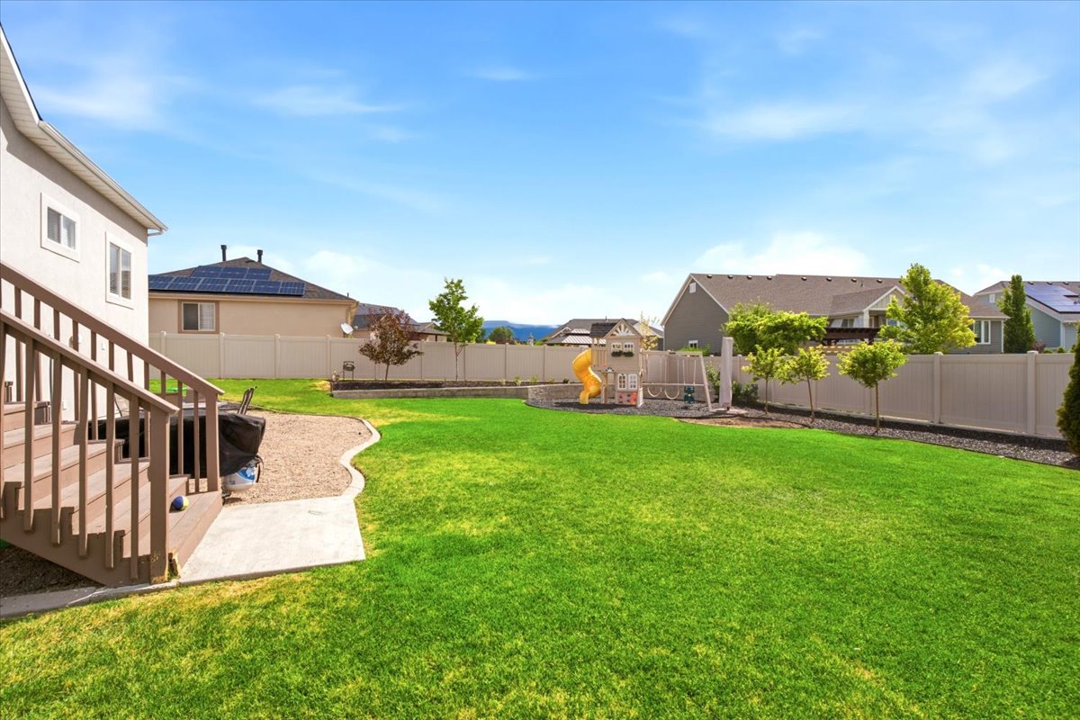 Expansive backyard featuring a lush green lawn, a multi-level composite deck, and a concrete patio area