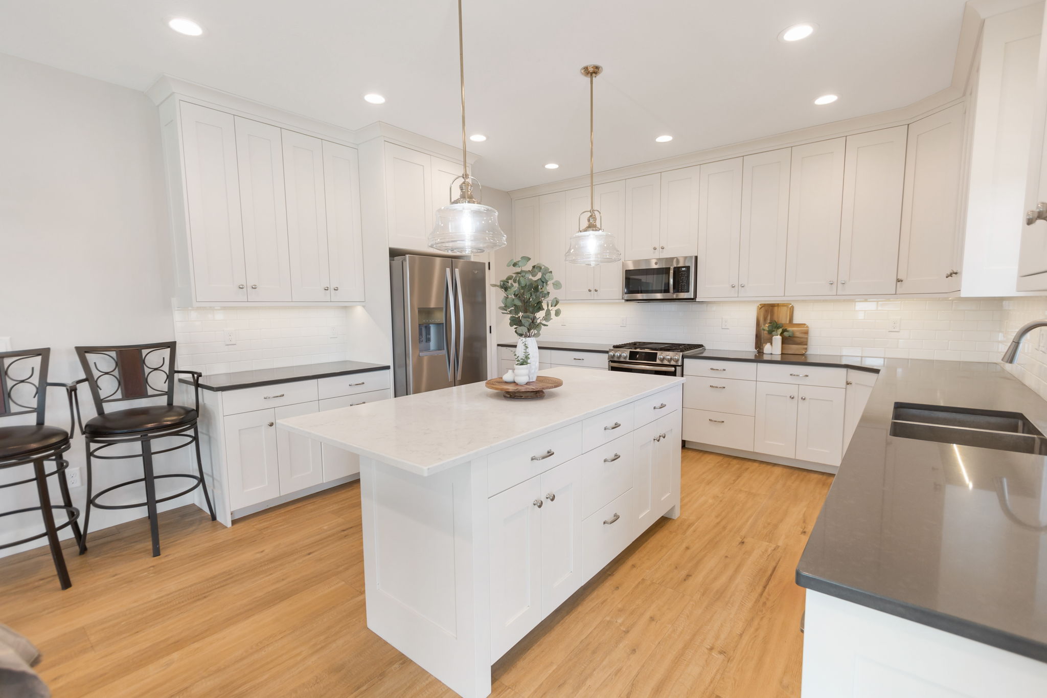 Modern kitchen featuring a large central island with seating, white shaker cabinetry, stainless steel appliances, and wood-finish flooring