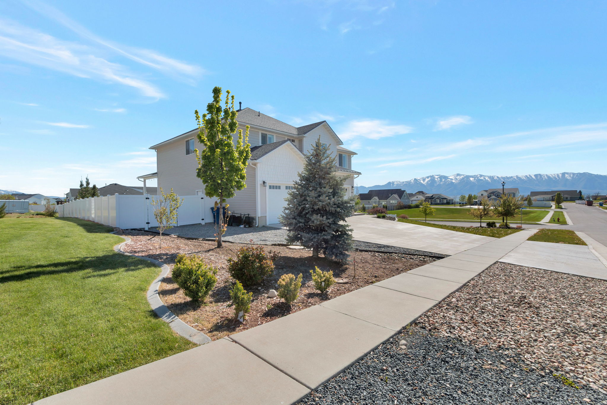 Light-toned two-story residence with attached garage, concrete driveway, and front yard landscaping