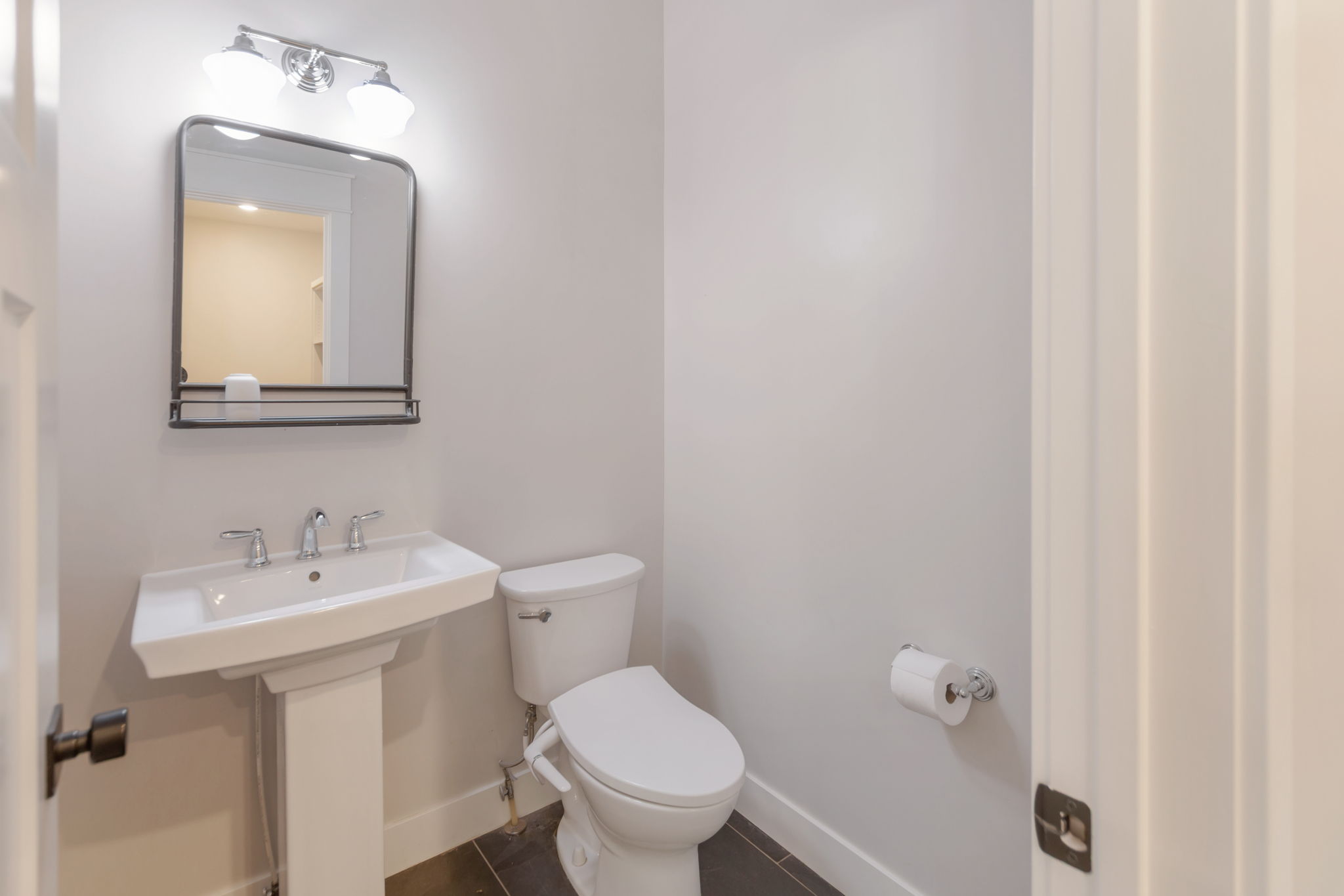 Pedestal sink with a polished chrome faucet, complemented by a rectangular framed mirror featuring a built-in shelf