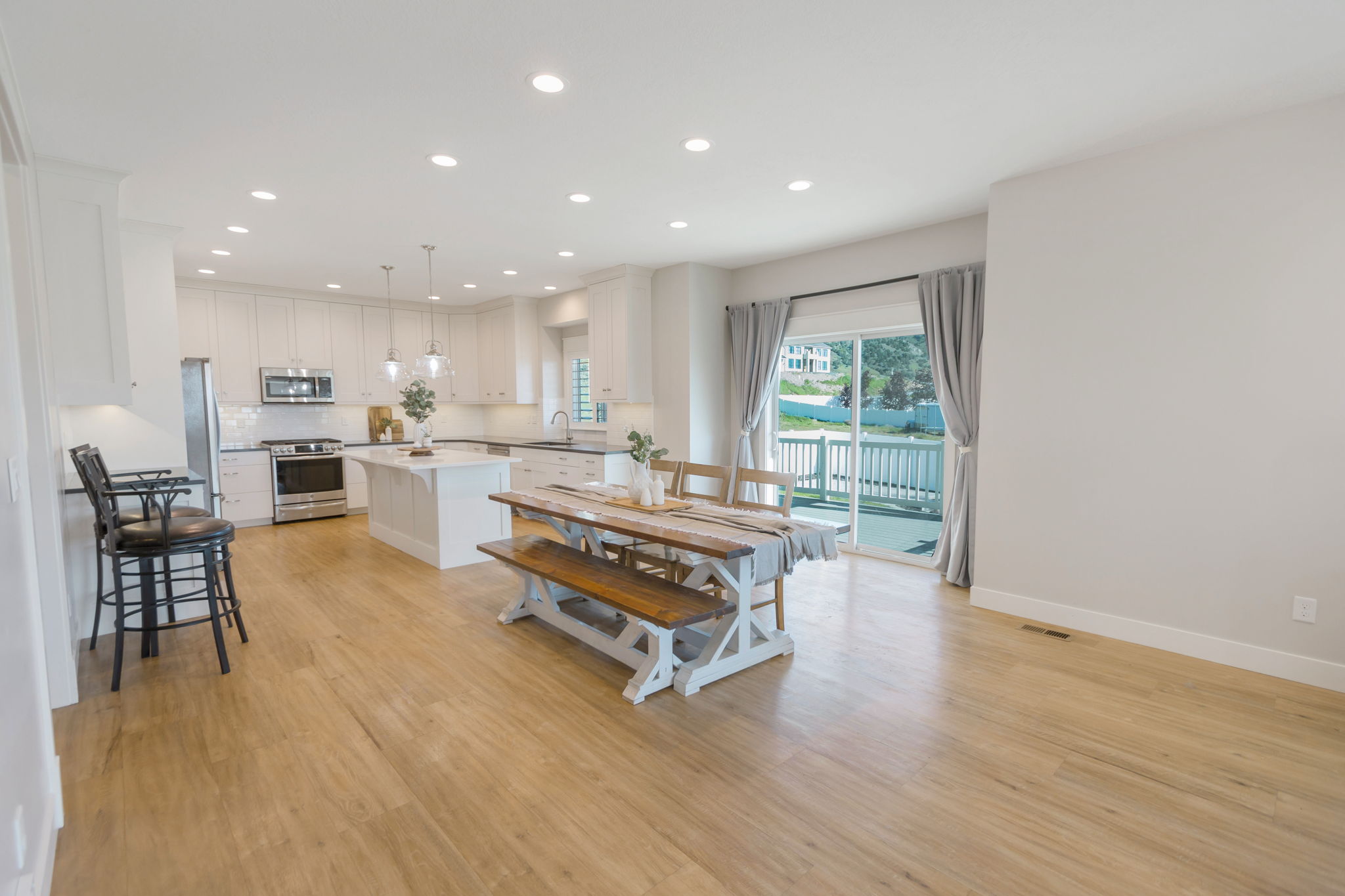 Open-concept living space featuring wood-finish flooring, a contemporary kitchen with white cabinetry, stainless steel appliances, and a central island with pendant lighting