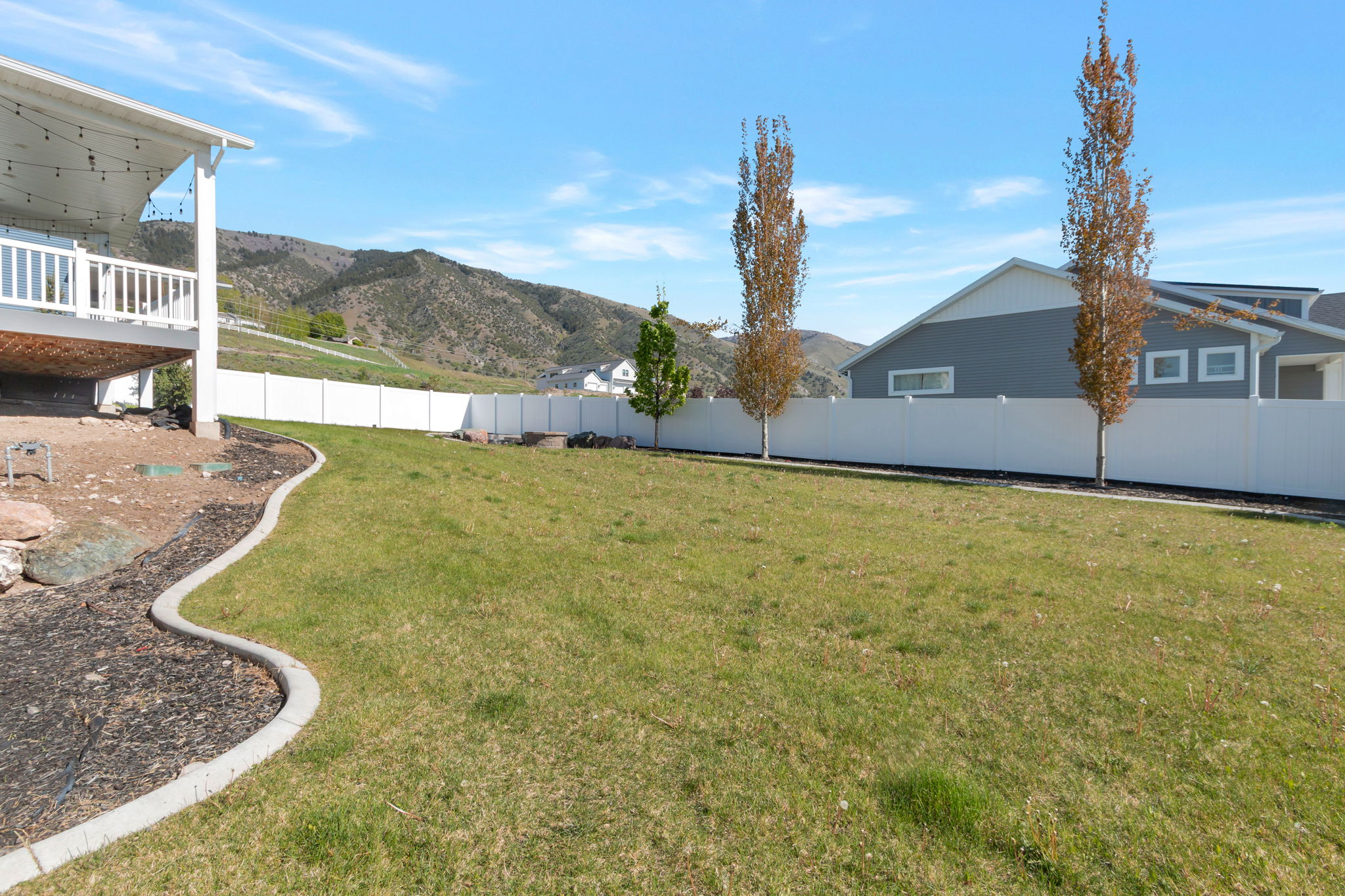 Expansive grassy yard with a concrete curbing border and a white privacy fence