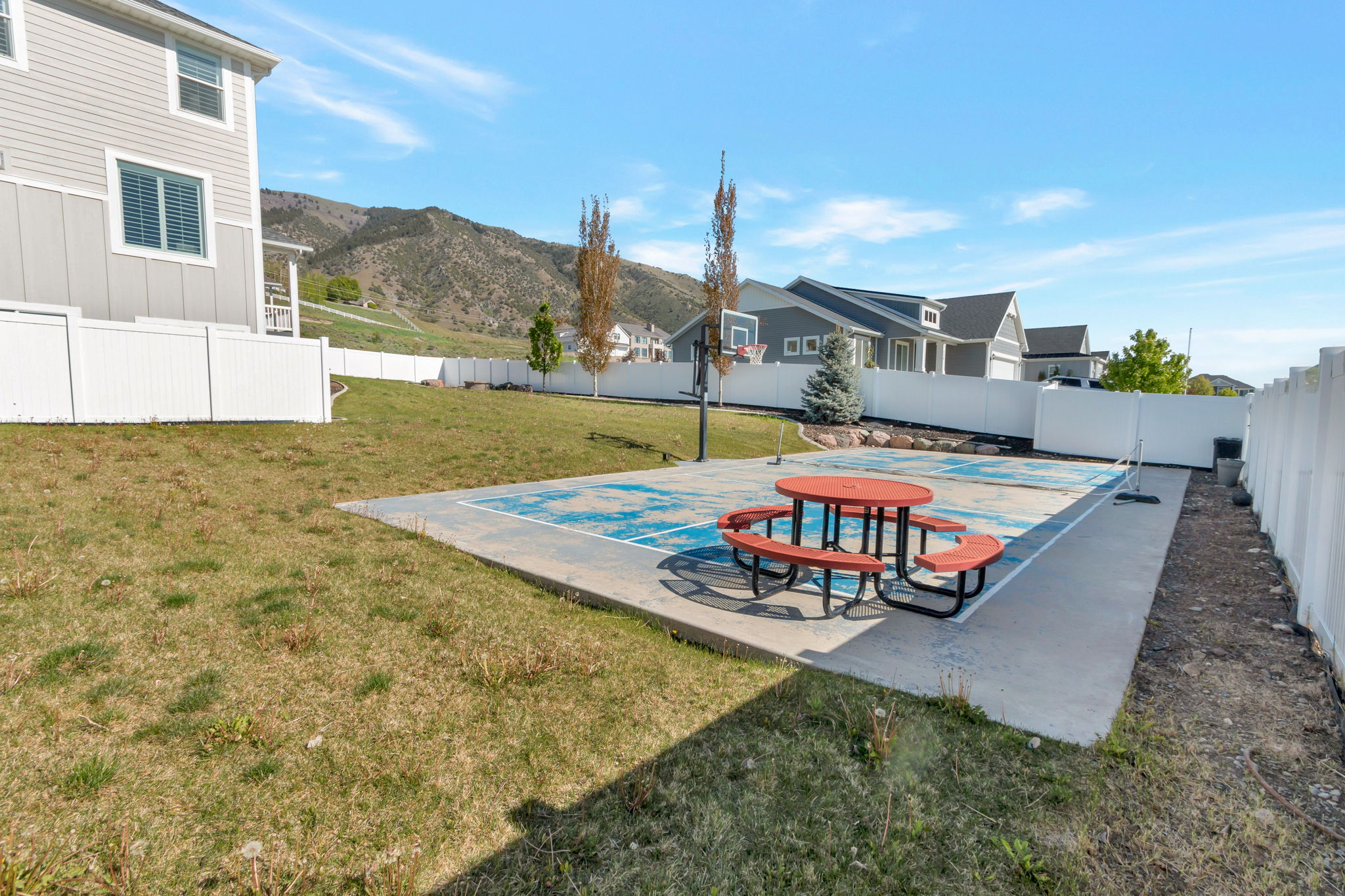 Backyard recreation space featuring a concrete sport court, white vinyl perimeter fencing, and a basketball hoop