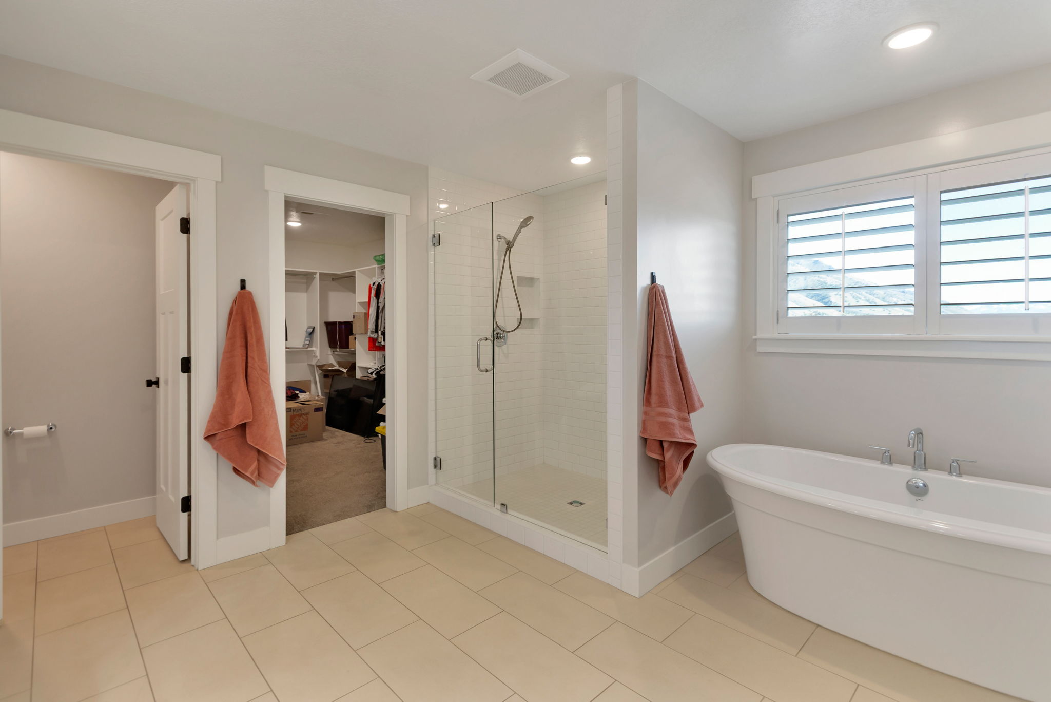 Bathroom featuring a freestanding tub, glass-enclosed shower, white tile flooring, and windows with white plantation shutters