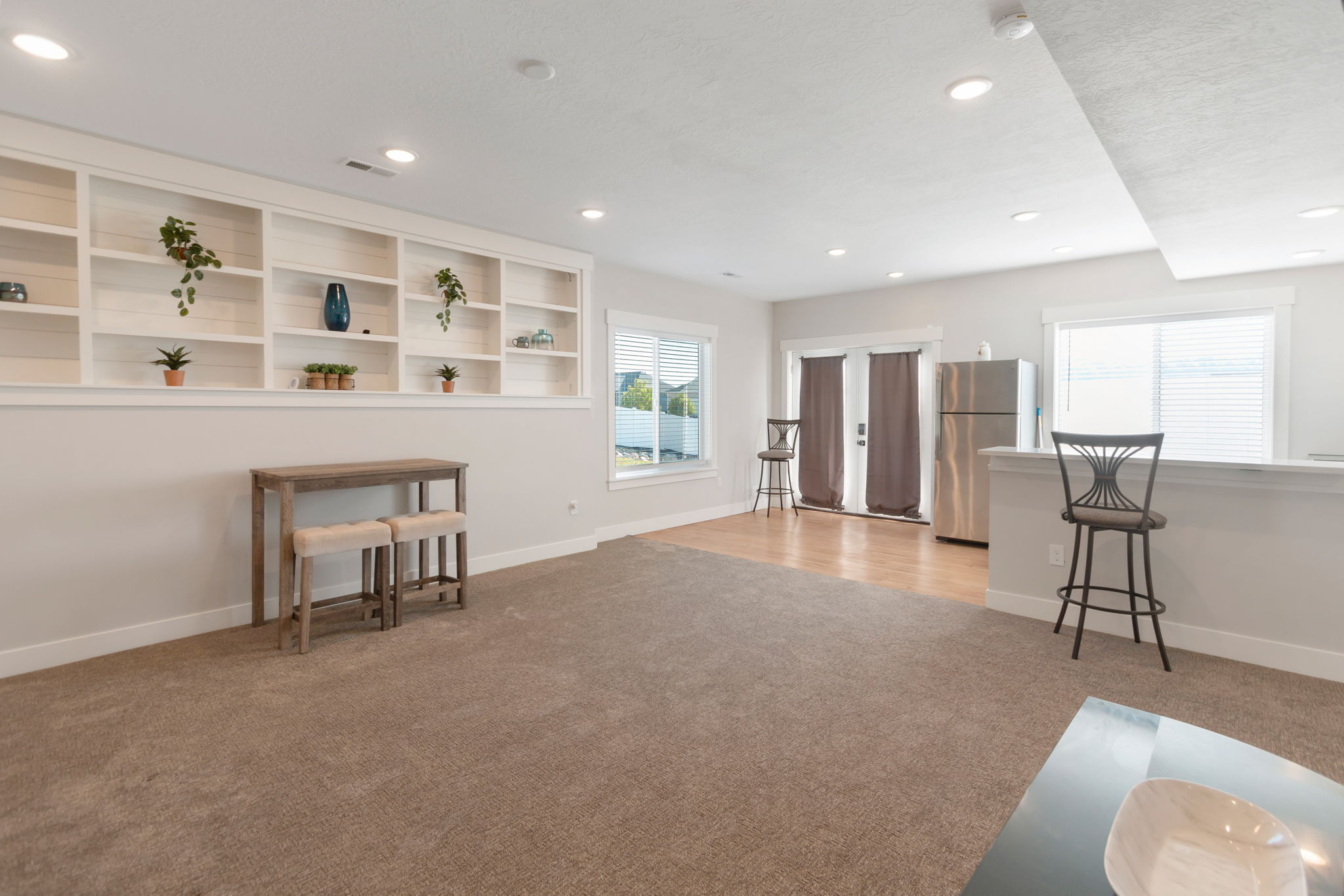 Expansive living area featuring plush carpet, recessed lighting, built-in shelving, durable wood-finish flooring, and a stainless steel refrigerator