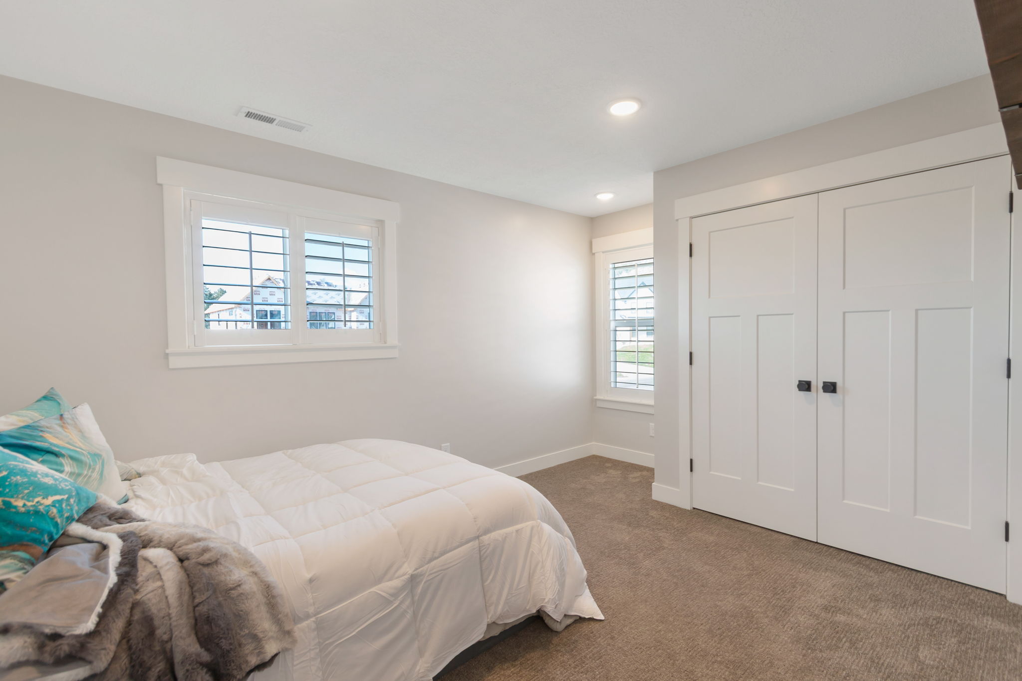 Bedroom featuring light gray walls, plush brown carpet, and a pair of white paneled closet doors with black hardware