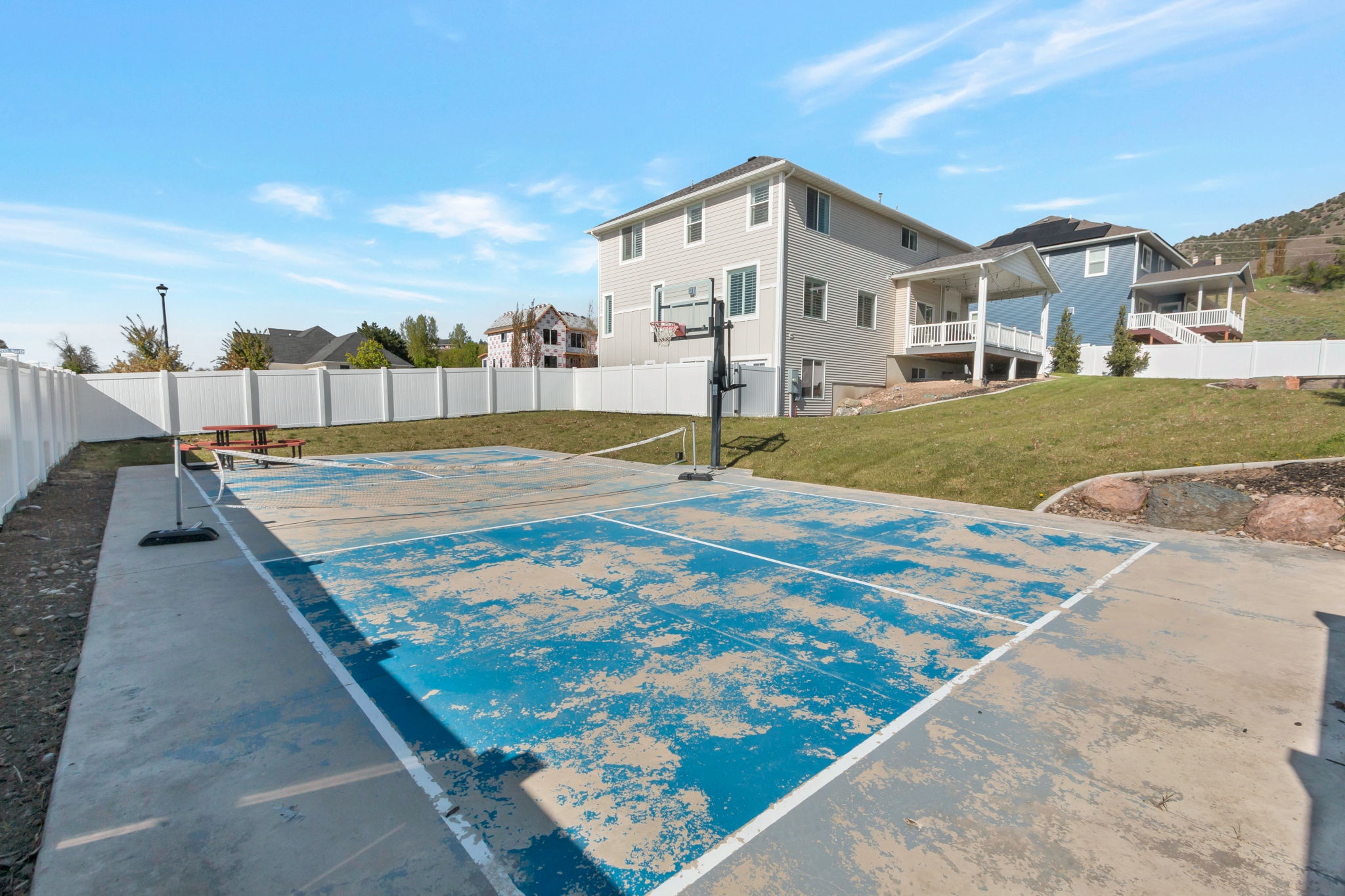 Outdoor concrete sport court with painted blue and white lines, featuring a basketball hoop and a tennis net