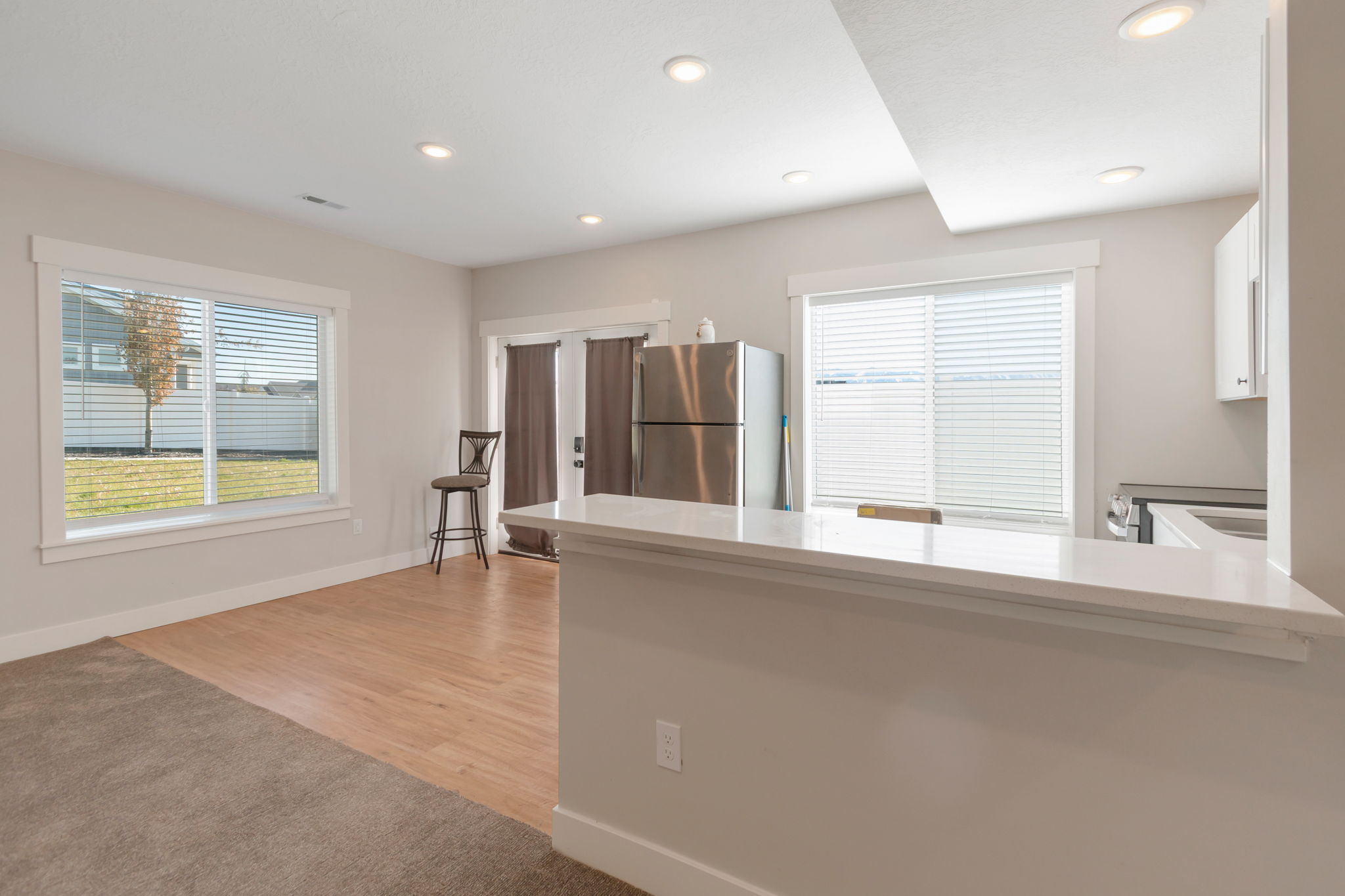 Open-concept living area featuring a kitchen island with a white countertop, recessed lighting, stainless steel appliances, and a glass-paned exterior door