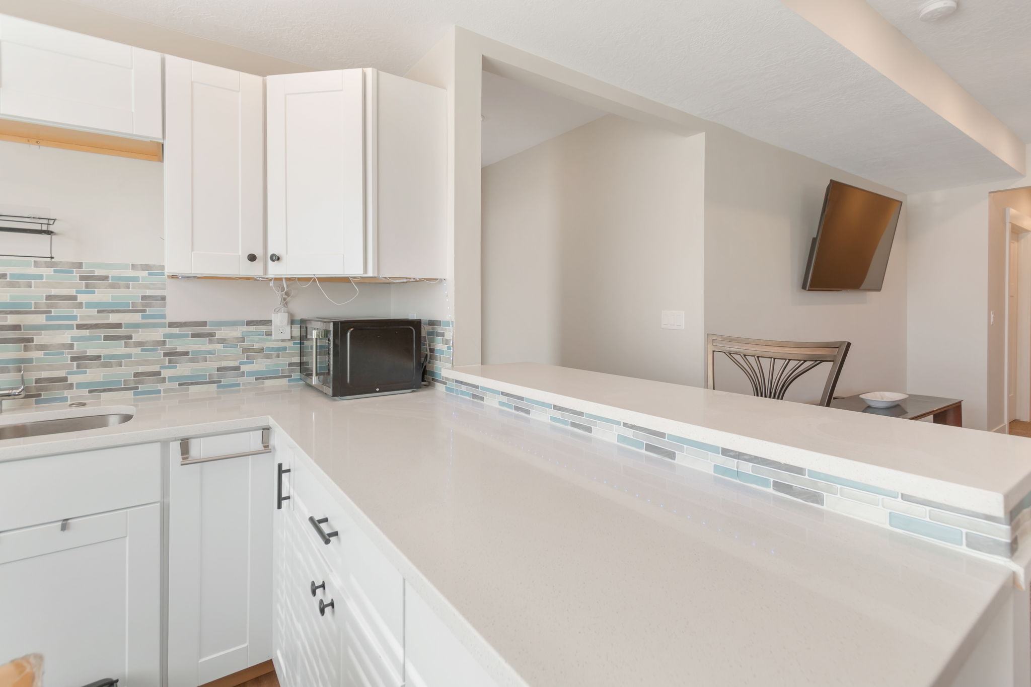 Kitchen featuring white cabinetry with dark hardware, a stainless steel sink, and a light-toned countertop