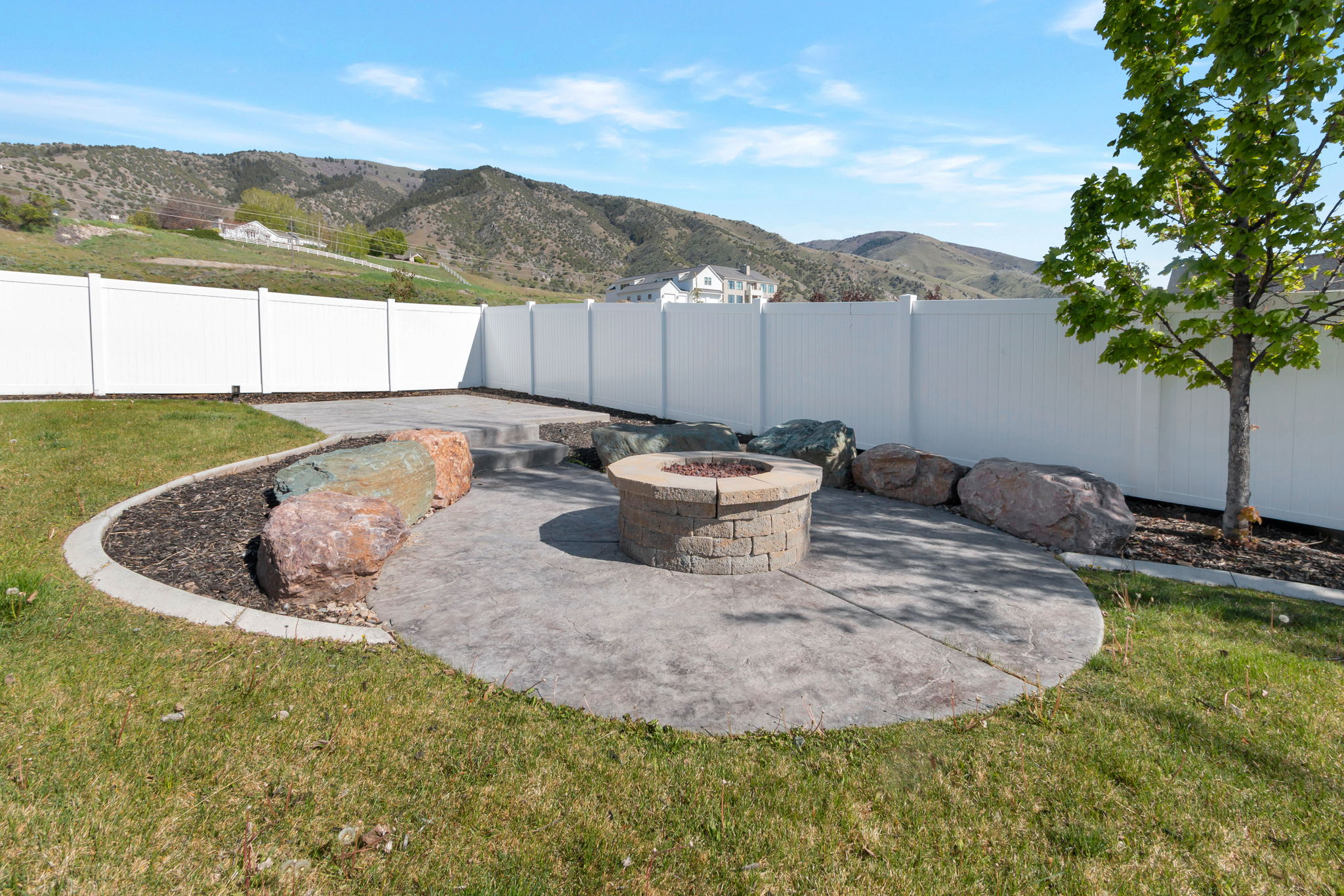 Outdoor living area featuring a stamped concrete patio, built-in stone fire pit, and decorative boulders