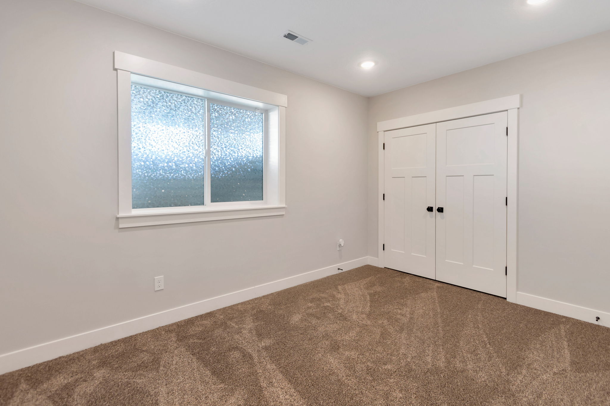 Neutral-toned room featuring a frosted window with white trim, a double-door closet with black hardware, and recessed ceiling lighting