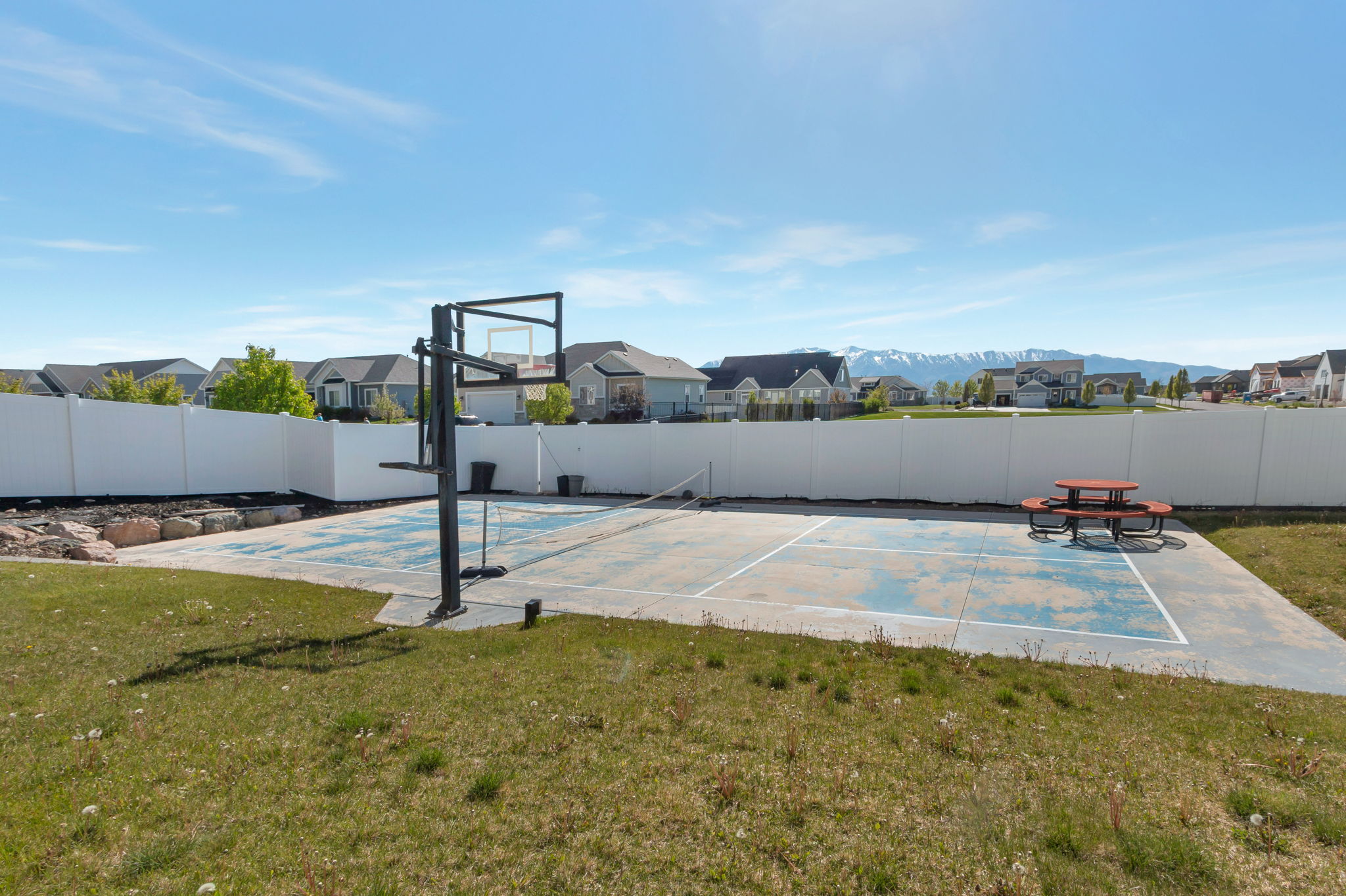 Outdoor sports court with a basketball hoop and net, surrounded by a white privacy fence