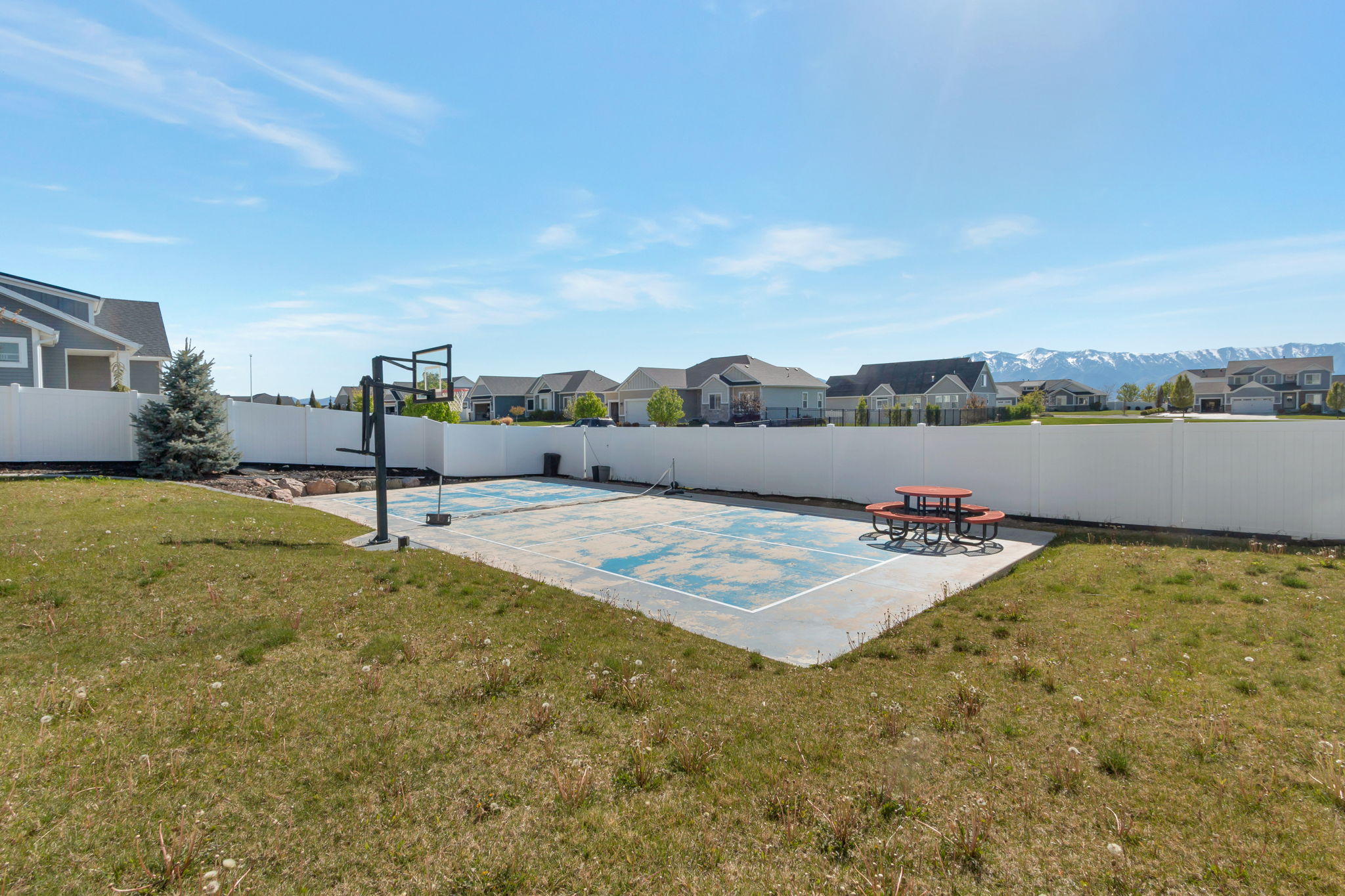 Expansive backyard featuring a multi-sport court with a basketball hoop, established lawn, and a white privacy fence