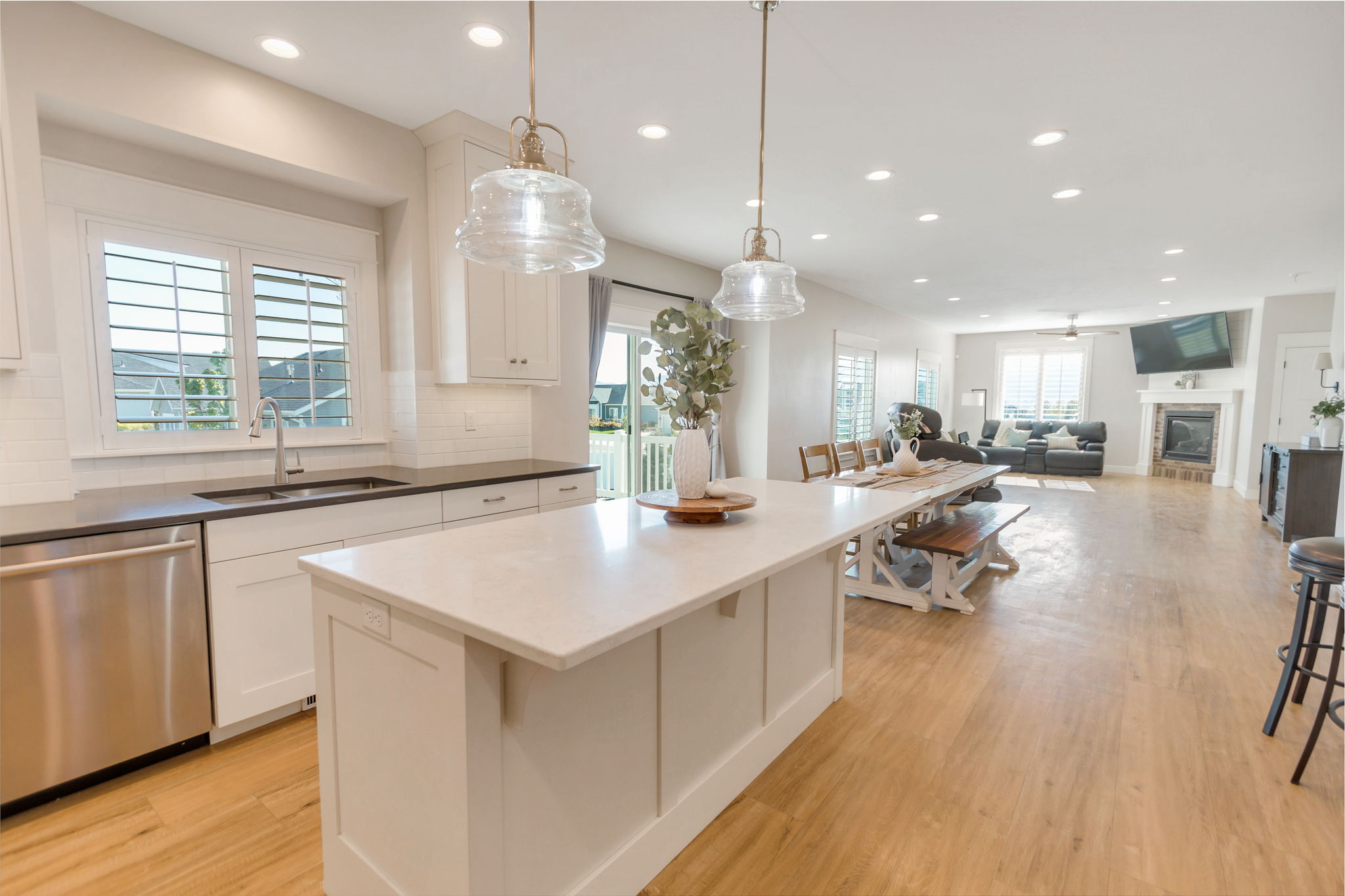 Open-concept kitchen and living area featuring a large center island, wood-finish flooring, white cabinetry, recessed lighting, and a fireplace with a mantel