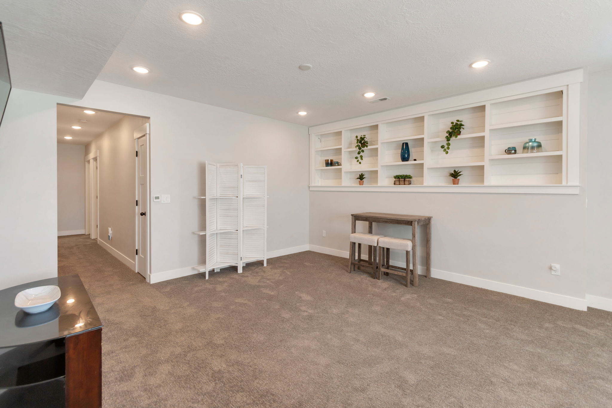 Spacious room featuring built-in shelving, recessed lighting, neutral-toned carpeting, light gray walls, and white baseboards