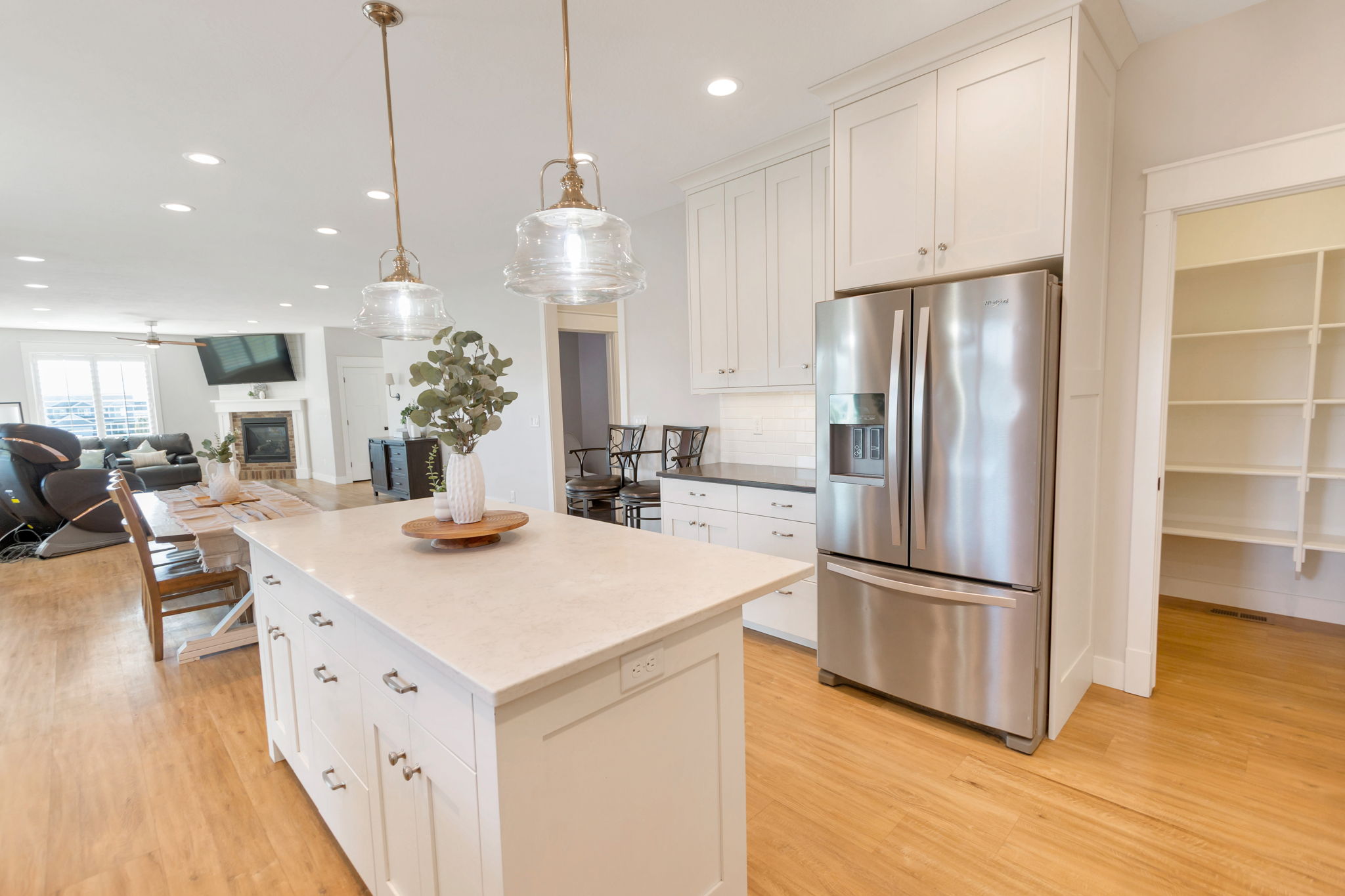Kitchen featuring a large island with a light-toned countertop, white cabinetry with silver-tone hardware, stainless steel refrigerator, and wood-finish flooring