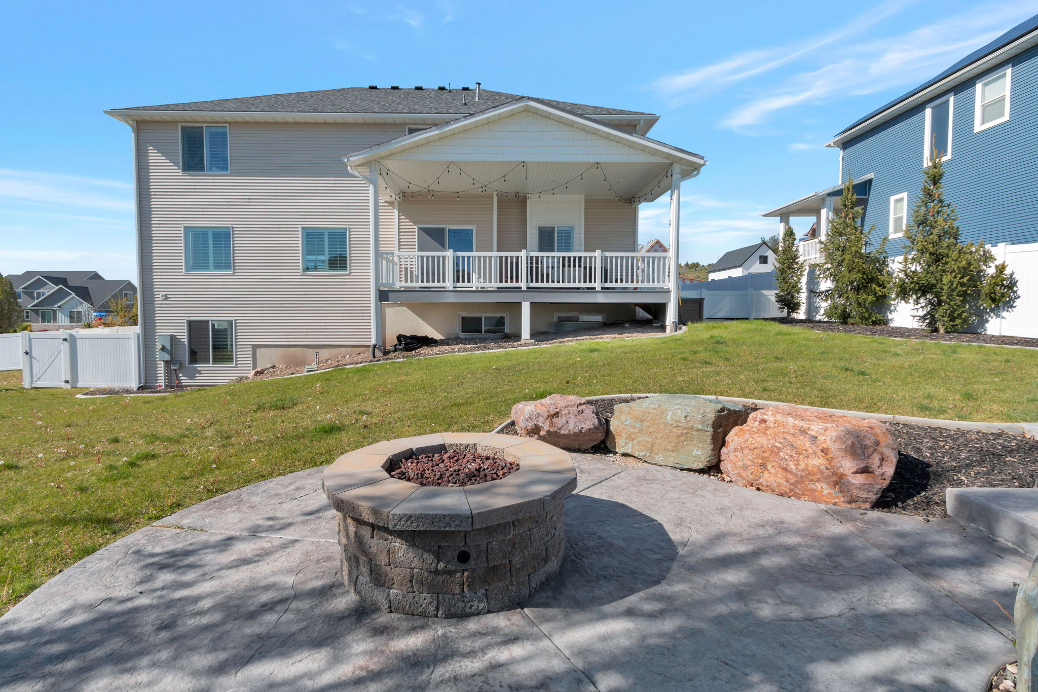 Stamped concrete patio featuring a built-in stone fire pit, surrounded by decorative boulders and landscaped beds