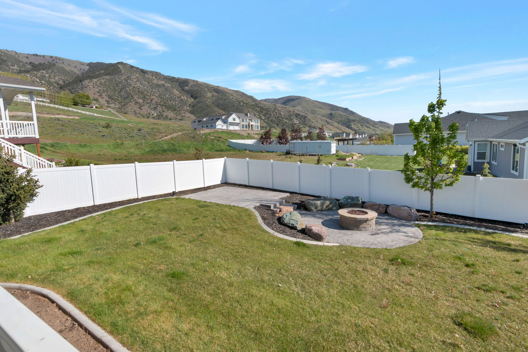 Expansive backyard featuring a circular paver patio with a built-in fire pit, surrounded by decorative boulders