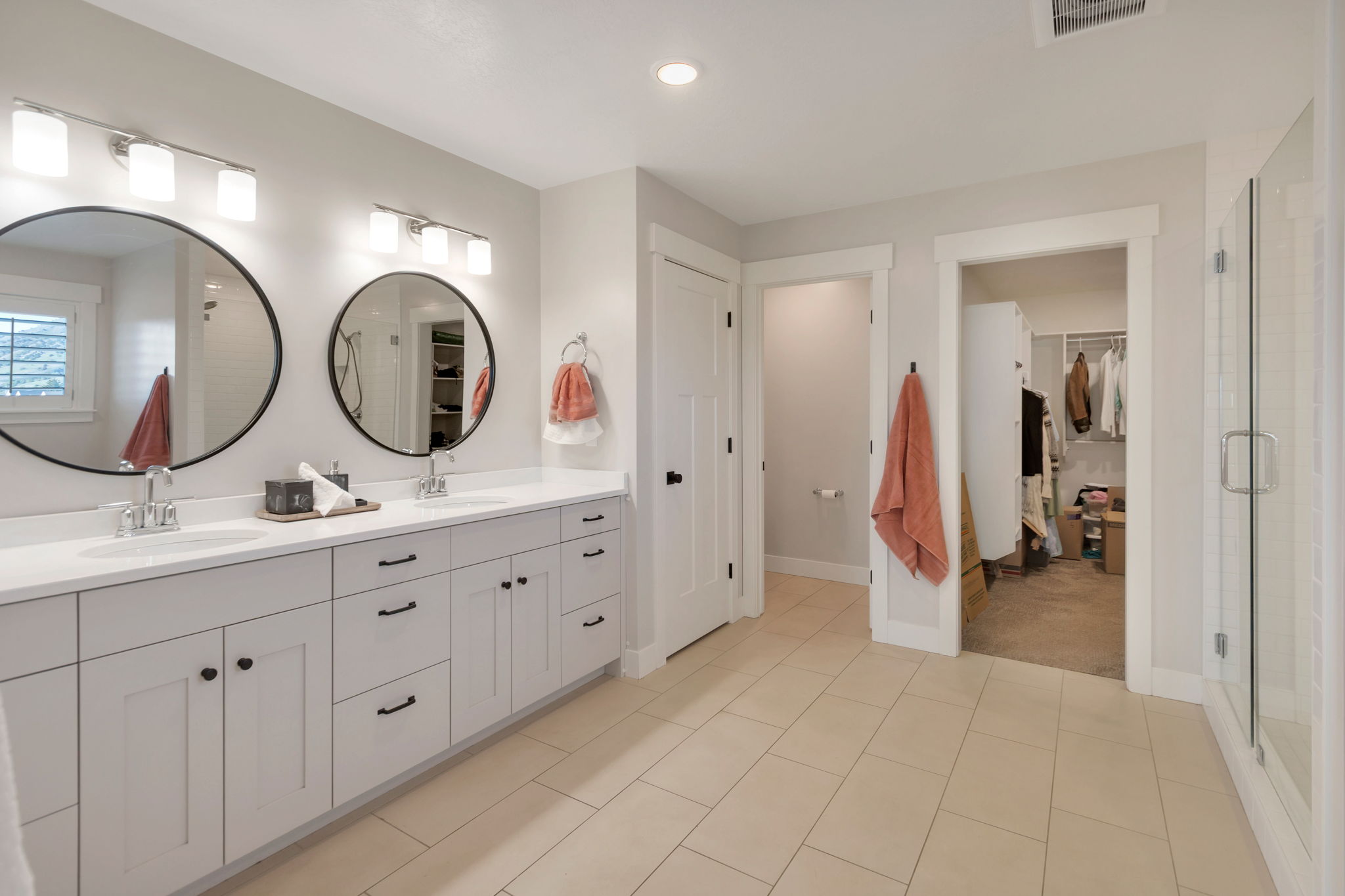 Spacious bathroom featuring a double vanity with white countertops, two round mirrors, and sconce lighting