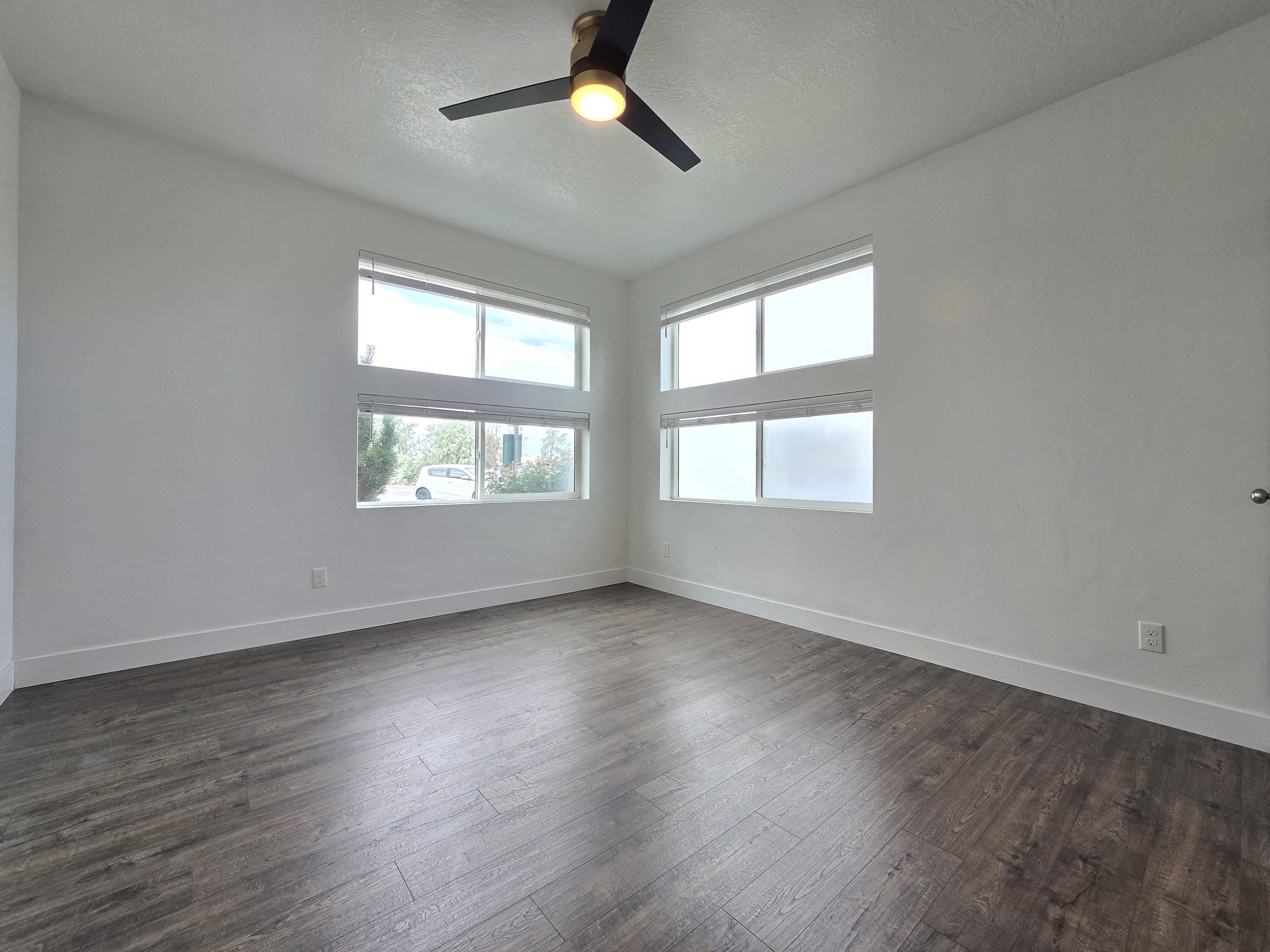 Spacious room featuring wood-finish flooring, white baseboards, and a modern ceiling fan