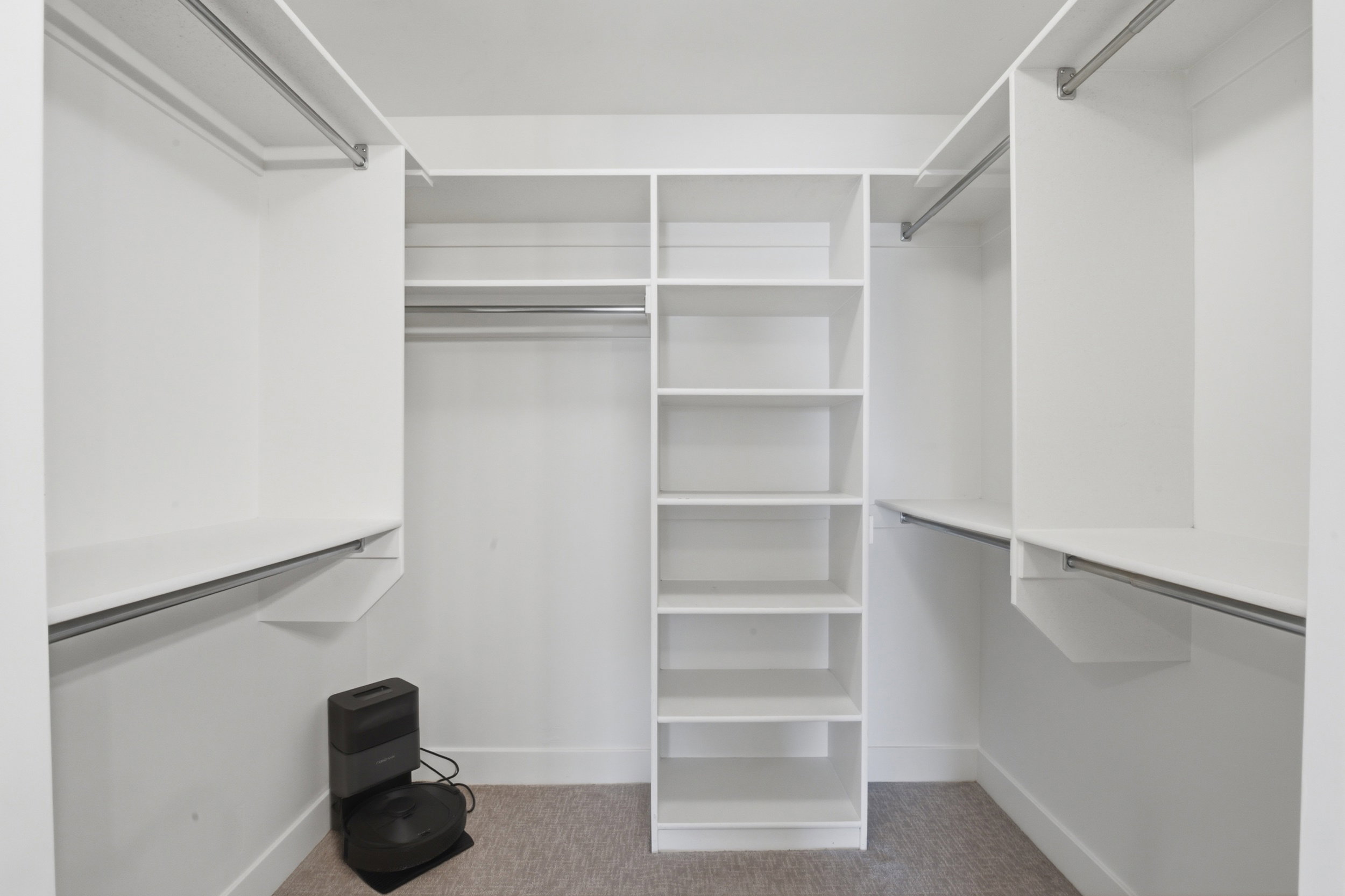 Primary bedroom walk-in closet featuring white built-in shelving, multiple hanging rods, and light-colored carpeting